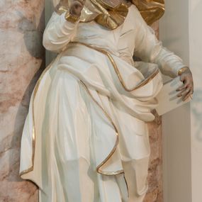 Zdjęcie nr 1: Rzeźba drążona z tyłu, ustawiona na niewielkiej podstawie. Święta zwrócona w trzech czwartych w prawo, w kontrapoście, lewa ręka przytrzymuje na boku księgę, prawa jest ugięta, uniesiona i wyciągnięta w bok. Twarz ma szczupłą, o wyraźnie podkreślonej linii żuchwy, migdałowatych, blisko siebie osadzonych oczach, dużym nosie i małych, rozchylonych ustach, okoloną włosami ukrytymi pod welonem. Ubrana jest w długą, białą tunikę ze złoconymi lamówkami, przylegającą do ciała w partii torsu oraz obfity, biały płaszcz ze złoconą lamówką zawinięty wokół bioder. Polichromia ciała naturalistyczna. 