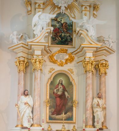 Zdjęcie nr 1: Nastawa architektoniczna, jednoosiowa, dwukondygnacyjna ze zwieńczeniem, ustawiona na dwustrefowym cokole. Ołtarz drewniany, prostopadłościenny z drewnianą mensą, w partii antepedium wyodrębnione zewnętrzne prostopadłościany, dekorowane płycinami. Na ołtarzu znajduje się tabernakulum w formie drewnianej skrzynki o wypukłym licu i wklęsłych bokach, ustawionej na cokole, flankowanej parą pilastrów o trzonach w formie spływów wolutowych oraz zewnętrzną parą kolumienek. Podpory dźwigają profilowany gzyms, na którym znajduje się tron wystawienia w formie cokołu. Drzwiczki w formie stojącego prostokąta z aplikowaną grupą Ukrzyżowania. Cokół dwustrefowy z wyodrębnionymi prostopadłościanami dekorowanymi w pierwszej strefie płycinami, w drugiej rocaille'owymi płycinami. Pierwsza kondygnacja flankowana dwiema parami pilastrów i stojących przed nimi kolumn ustawionych na cokołach, druga para zwrócona pod kątem na zewnątrz. Podpory dźwigają wyłamane na ich osi fragmenty belkowania, środkowa para również przerwany, falisty przyczółek. Na belkowaniu i przyczółku siedzi para puttów i para adorujących aniołów. Pomiędzy parami kolumn ustawione figury, u dołu z kartuszami z napisami „św(ięty) Piotr” i „św(ięty) Paweł”. W polu głównym znajduje się wnęka w formie stojącego prostokąta zamkniętego łukiem półkolistym nadwieszonym z uskokiem, ujęta profilowaną ramą z obrazem Najświętszego Serca Jezusa. Ponad obrazem kartusz ujęty stylizowanym rocaille'em z napisem „NAJŚWIĘTSZE / SERCE JEZUSA / ZMIŁUJ SIĘ / NAD NAMI”. Druga kondygnacja flankowana dwiema parami pilastrów, w tym zewnętrzną ustawioną pod kątem, o trzonach przechodzących w woluty spływające na cokoły na belkowaniu pierwszej kondygnacji nastawy. Podpory dźwigają gzyms przerwany na polem. Całość zamknięta medalionem z monogramem IHS otoczonym wieńcem z obłoków i uskrzydlonych główek anielskich, w glorii promienistej. U dołu medalionu i na gzymsie znajdują się putta. W polu wnęka w formie stojącego prostokąta zamkniętego łukiem półkolistym nadwieszonym w ramie, z obrazem św. Jerzego walczącego ze smokiem. Struktura niemal w całości polichromowana w kolorze białym, trzony kolumn polichromowane na sposób imitujący marmoryzację w kolorze biało-różowym, profile i ornamentyka złocone. 