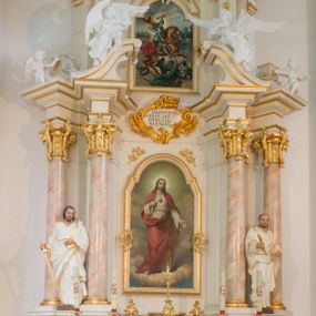 Zdjęcie nr 1: Nastawa architektoniczna, jednoosiowa, dwukondygnacyjna ze zwieńczeniem, ustawiona na dwustrefowym cokole. Ołtarz drewniany, prostopadłościenny z drewnianą mensą, w partii antepedium wyodrębnione zewnętrzne prostopadłościany, dekorowane płycinami. Na ołtarzu znajduje się tabernakulum w formie drewnianej skrzynki o wypukłym licu i wklęsłych bokach, ustawionej na cokole, flankowanej parą pilastrów o trzonach w formie spływów wolutowych oraz zewnętrzną parą kolumienek. Podpory dźwigają profilowany gzyms, na którym znajduje się tron wystawienia w formie cokołu. Drzwiczki w formie stojącego prostokąta z aplikowaną grupą Ukrzyżowania. Cokół dwustrefowy z wyodrębnionymi prostopadłościanami dekorowanymi w pierwszej strefie płycinami, w drugiej rocaille'owymi płycinami. Pierwsza kondygnacja flankowana dwiema parami pilastrów i stojących przed nimi kolumn ustawionych na cokołach, druga para zwrócona pod kątem na zewnątrz. Podpory dźwigają wyłamane na ich osi fragmenty belkowania, środkowa para również przerwany, falisty przyczółek. Na belkowaniu i przyczółku siedzi para puttów i para adorujących aniołów. Pomiędzy parami kolumn ustawione figury, u dołu z kartuszami z napisami „św(ięty) Piotr” i „św(ięty) Paweł”. W polu głównym znajduje się wnęka w formie stojącego prostokąta zamkniętego łukiem półkolistym nadwieszonym z uskokiem, ujęta profilowaną ramą z obrazem Najświętszego Serca Jezusa. Ponad obrazem kartusz ujęty stylizowanym rocaille'em z napisem „NAJŚWIĘTSZE / SERCE JEZUSA / ZMIŁUJ SIĘ / NAD NAMI”. Druga kondygnacja flankowana dwiema parami pilastrów, w tym zewnętrzną ustawioną pod kątem, o trzonach przechodzących w woluty spływające na cokoły na belkowaniu pierwszej kondygnacji nastawy. Podpory dźwigają gzyms przerwany na polem. Całość zamknięta medalionem z monogramem IHS otoczonym wieńcem z obłoków i uskrzydlonych główek anielskich, w glorii promienistej. U dołu medalionu i na gzymsie znajdują się putta. W polu wnęka w formie stojącego prostokąta zamkniętego łukiem półkolistym nadwieszonym w ramie, z obrazem św. Jerzego walczącego ze smokiem. Struktura niemal w całości polichromowana w kolorze białym, trzony kolumn polichromowane na sposób imitujący marmoryzację w kolorze biało-różowym, profile i ornamentyka złocone. 