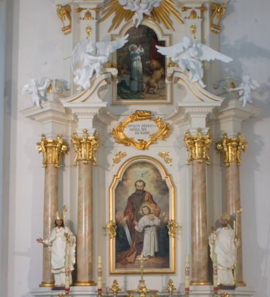 Zdjęcie nr 1: Nastawa architektoniczna, jednoosiowa, dwukondygnacyjna ze zwieńczeniem, ustawiona na dwustrefowym cokole. Ołtarz drewniany, prostopadłościenny z drewnianą mensą, w partii antepedium wyodrębnione zewnętrzne prostopadłościany, dekorowane płycinami. Na ołtarzu znajduje się tabernakulum w formie drewnianej skrzynki o wypukłym licu i wklęsłych bokach, ustawionej na cokole, flankowanej parą pilastrów o trzonach w formie spływów wolutowych oraz zewnętrzną parą kolumienek. Podpory dźwigają profilowany gzyms, na którym znajduje się tron wystawienia w formie cokołu. Drzwiczki w formie stojącego prostokąta z aplikowaną sceną Chrystusa w świątyni. Cokół dwustrefowy z wyodrębnionymi prostopadłościanami dekorowanymi w pierwszej strefie płycinami, w drugiej rocaille&#039;owymi płycinami. Pierwsza kondygnacja flankowana dwiema parami pilastrów i stojących przed nimi kolumn ustawionych na cokołach, druga para zwrócona pod kątem na zewnątrz. Podpory dźwigają wyłamane na ich osi fragmenty belkowania, środkowa para również przerwany, falisty przyczółek. Na belkowaniu i przyczółku siedzi para puttów i para adorujących aniołów. Pomiędzy parami kolumn ustawione figury, u dołu z kartuszami z napisami „św(ięty) Stanisław” i „św(ięty) Wojciech”. W polu głównym znajduje się wnęka w formie stojącego prostokąta zamkniętego łukiem półkolistym nadwieszonym z uskokiem, ujęta profilowaną ramą z obrazem św. Józefa z małym Jezusem. Ponad obrazem kartusz ujęty stylizowanym rocaille&#039;em z napisem „ŚWIĘTY JÓZEFIE / MÓDL SIĘ / ZA NAMI”. Druga kondygnacja flankowane dwiema parami pilastrów, w tym zewnętrzną ustawioną pod kątem na zewnątrz o trzonach przechodzących w woluty spływające na cokoły na belkowaniu pierwszej kondygnacji nastawy. Podpory dźwigają gzyms przerwany na polem. Całość zamknięta medalionem z gołębicą Ducha Świętego w glorii, otoczonym wieńcem z obłoków i uskrzydlonych główek anielskich, w glorii promienistej. U dołu medalionu i na gzymsie znajdują się putta. W polu wnęka w formie stojącego prostokąta zamkniętego łukiem półkolistym nadwieszonym w ramie, z obrazem św. Ignacego Antiocheńskiego. Struktura niemal w całości polichromowana w kolorze białym, trzony kolumn polichromowane na sposób imitujący marmoryzację w kolorze biało-różowym, profile i ornamentyka złocone. 