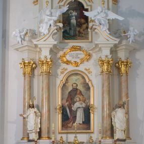 Zdjęcie nr 1: Nastawa architektoniczna, jednoosiowa, dwukondygnacyjna ze zwieńczeniem, ustawiona na dwustrefowym cokole. Ołtarz drewniany, prostopadłościenny z drewnianą mensą, w partii antepedium wyodrębnione zewnętrzne prostopadłościany, dekorowane płycinami. Na ołtarzu znajduje się tabernakulum w formie drewnianej skrzynki o wypukłym licu i wklęsłych bokach, ustawionej na cokole, flankowanej parą pilastrów o trzonach w formie spływów wolutowych oraz zewnętrzną parą kolumienek. Podpory dźwigają profilowany gzyms, na którym znajduje się tron wystawienia w formie cokołu. Drzwiczki w formie stojącego prostokąta z aplikowaną sceną Chrystusa w świątyni. Cokół dwustrefowy z wyodrębnionymi prostopadłościanami dekorowanymi w pierwszej strefie płycinami, w drugiej rocaille'owymi płycinami. Pierwsza kondygnacja flankowana dwiema parami pilastrów i stojących przed nimi kolumn ustawionych na cokołach, druga para zwrócona pod kątem na zewnątrz. Podpory dźwigają wyłamane na ich osi fragmenty belkowania, środkowa para również przerwany, falisty przyczółek. Na belkowaniu i przyczółku siedzi para puttów i para adorujących aniołów. Pomiędzy parami kolumn ustawione figury, u dołu z kartuszami z napisami „św(ięty) Stanisław” i „św(ięty) Wojciech”. W polu głównym znajduje się wnęka w formie stojącego prostokąta zamkniętego łukiem półkolistym nadwieszonym z uskokiem, ujęta profilowaną ramą z obrazem św. Józefa z małym Jezusem. Ponad obrazem kartusz ujęty stylizowanym rocaille'em z napisem „ŚWIĘTY JÓZEFIE / MÓDL SIĘ / ZA NAMI”. Druga kondygnacja flankowane dwiema parami pilastrów, w tym zewnętrzną ustawioną pod kątem na zewnątrz o trzonach przechodzących w woluty spływające na cokoły na belkowaniu pierwszej kondygnacji nastawy. Podpory dźwigają gzyms przerwany na polem. Całość zamknięta medalionem z gołębicą Ducha Świętego w glorii, otoczonym wieńcem z obłoków i uskrzydlonych główek anielskich, w glorii promienistej. U dołu medalionu i na gzymsie znajdują się putta. W polu wnęka w formie stojącego prostokąta zamkniętego łukiem półkolistym nadwieszonym w ramie, z obrazem św. Ignacego Antiocheńskiego. Struktura niemal w całości polichromowana w kolorze białym, trzony kolumn polichromowane na sposób imitujący marmoryzację w kolorze biało-różowym, profile i ornamentyka złocone. 