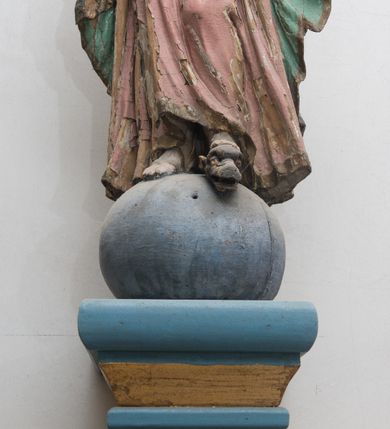 Zdjęcie nr 2: Figura ustawiona na kuli. Maria zwrócona w trzech czwartych w prawo, w kontrapoście, lewą stopą depcze głowę węża, ręce ma skrzyżowane na piersi. Twarz ma owalną, o małych oczach skierowanych w dół, niewielkim nosie i ustach, okoloną długimi włosami, opadającymi na ramiona. Ubrana jest w różową suknię o złoconych lamówkach, obficie fałdowaną, przewiązaną w talii. Na głowę i ramiona ma narzucony zielony płaszcz ze złoconą lamówką, opadający wzdłuż boków i zawieszony na prawym przedramieniu. Polichromia ciała naturalistyczna. 