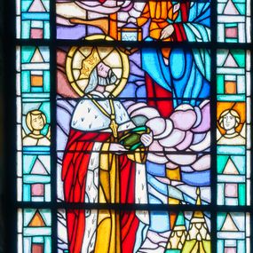 Zdjęcie nr 1: Witraż w kształcie stojącego prostokąta zamkniętego łukiem pełnym w szerokiej bordiurze wypełnionej popiersiami aniołów i figurami geometrycznymi. W centrum scena, w której św. Ludwik prezentuje koronę cierniową Matce Boskiej z Dzieciątkiem. Król obiema rękami przytrzymuje atrybut męki, głowę unosi w kierunku świętych. Ma długie, siwe włosy, taką samą brodę i wąsy. Jest ubrany w fioletową albę, żółtą komżę i obszerny płaszcz królewski lamowany gronostajem, z futrzaną pelerynką. Na szyi ma złoty krzyż, na głowie koronę. W wyższej partii kompozycji, po prawej stronie przedstawiono Matkę Boską tronującą pośród chmur i trzymającą na prawym kolanie Dzieciątko, które lewą rękę wyciąga w jej kierunku, a w prawej trzyma tarczę herbową z trzeba liliami. Maria ma ciemną karnację,  jest ubrana w czerwoną suknię i niebieski maforion. Dzieciątko ma na sobie pomarańczową tunikę przewiązaną w pasie. Głowy wszystkich postaci otaczają nimby. Na drugim planie widoczne rozbite namioty – żółty i zielony, dalej mury miast. W górnej partii otoczony różowo-fioletowymi chmurami napis „ŚW. / LUD/WIK”, w partii bordiury, przy dolnej krawędzi „FUNDACJA / DR STANISŁAW / SĘK”.