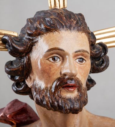 Zdjęcie nr 3: Rzeźba pełna, ustawiona na profilowanym cokole i na rzeźbionej skale. Chrystus zwrócony jest frontalnie, z głową skierowaną w lewą stronę, stoi w silnym kontrapoście. W prawej, uniesionej ręce trzyma drzewce zakończone krzyżem z chorągwią z tkaniny lamowanej koronką, z haftowanym monogramem IHS w glorii, lewą zaś wyciąga w bok. Twarz ma szczupłą, o głęboko osadzonych migdałowatych oczach, niewielkim nosie i małych, pełnych ustach, okoloną brodą oraz krótkimi włosami zaczesanymi do tyłu, układającymi się po bokach w silnie skręcone pukle. Z jego głowy wychodzą trzy wiązki promieni. Chrystus ma przepasane biodra posrebrzonym perizonium. Na prawym ramieniu, na pasku ma zawieszony silnie drapowany i ekspresyjne rozwiany bladoczerwony płaszcz z błękitną podszewką, zarzucony na plecy i na ugiętą prawą nogę. Jego ciało jest szczupłe, o delikatnie zarysowanej, miękko modelowanej muskulaturze torsu i ramion, z zaznaczonymi śladami męki. Na odwrocie podstawy inskrypcja „A(NNO) D(OMINI) / 1781 / A(ntoni) Kornec/ki”. 