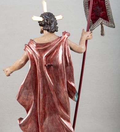 Zdjęcie nr 8: Rzeźba pełna, ustawiona na profilowanym cokole i na rzeźbionej skale. Chrystus zwrócony jest frontalnie, z głową skierowaną w lewą stronę, stoi w silnym kontrapoście. W prawej, uniesionej ręce trzyma drzewce zakończone krzyżem z chorągwią z tkaniny lamowanej koronką, z haftowanym monogramem IHS w glorii, lewą zaś wyciąga w bok. Twarz ma szczupłą, o głęboko osadzonych migdałowatych oczach, niewielkim nosie i małych, pełnych ustach, okoloną brodą oraz krótkimi włosami zaczesanymi do tyłu, układającymi się po bokach w silnie skręcone pukle. Z jego głowy wychodzą trzy wiązki promieni. Chrystus ma przepasane biodra posrebrzonym perizonium. Na prawym ramieniu, na pasku ma zawieszony silnie drapowany i ekspresyjne rozwiany bladoczerwony płaszcz z błękitną podszewką, zarzucony na plecy i na ugiętą prawą nogę. Jego ciało jest szczupłe, o delikatnie zarysowanej, miękko modelowanej muskulaturze torsu i ramion, z zaznaczonymi śladami męki. Na odwrocie podstawy inskrypcja „A(NNO) D(OMINI) / 1781 / A(ntoni) Kornec/ki”. 