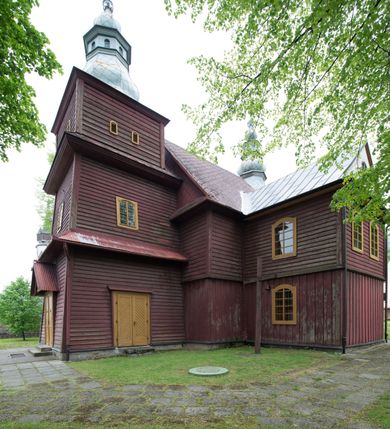 Zdjęcie nr 9: Kościół drewniany o konstrukcji zrębowej, na betonowym podmurowaniu przesłoniętym daszkiem, wieża o konstrukcji słupowej. Elewacje jednolite, szalowane w dolnej połowie pionowo, w górnej połowie poziomo, wzmocnione lisicami. Więźba dachowa drewniana, krokwiowa. Kościół orientowany, jednonawowy, nawa na rzucie prostokąta, prezbiterium nieco węższe, zakończone trójbocznie. Do wschodniej ściany prezbiterium przylega Ogrójec na rzucie prostokąta, od północy piętrowa zakrystia na planie prostokąta z niewielką prostokątną przybudówką od północy. Do zachodniej ściany nawy przylega wieża na planie kwadratu, do południowej ściany nawy kaplica na takim samym planie. 
Pomiędzy nawą a prezbiterium prostokątny otwór tęczowy. Wewnątrz ściany wzmocnione parami lizen, zakończone opasującym całość wnętrza profilowanym gzymsem. Parapet chóru muzycznego w zachodniej części nawy, o wypukłej środkowej części, podparty na czterech filarach. Zakrystia dwupiętrowa ze strychem, na drugim piętrze dawna loża kolatorska otwarta do wnętrza prezbiterium arkadą. Kaplica boczna dwupiętrowa, górne pomieszczenie dzielą od wnętrza dwa okna. Otwory drzwiowe o prostokątnym wykroju, zamknięte drzwiami spągowymi w południowej ścianie nawy oraz prezbiterium, drzwi w zachodniej ścianie dwuskrzydłowe. Wnętrze nakryte pułapami deskowymi o zaokrąglonych fasetach. Posadzka z płyt ceramicznych. 
Elewacja frontowa z dostawioną trójkondygnacyjną, zwężającą się ku górze wieżą, każda kondygnacja oddzielona daszkiem. Na osi oraz na południowej ścianie wejścia do kruchty w przyziemiu wieży z dwuskrzydłowymi drzwiami, frontowe nakryte dwuspadowym daszkiem z niszą na figurę Najświętszego Serca Jezusa. Prostokątne okna z dwóch stron pierwszej kondygnacji, trzech stron drugiej kondygnacji, w partii trzeciej z każdej strony para otworów dzwonnych. W elewacji północnej pięć otworów okiennych w formie stojącego prostokąta, dwa w nawie, po jednym w każdej kondygnacji zakrystii oraz w północnej przybudówce zakrystii wejście i małe prostokątne okienko. W elewacji południowej cztery okna w formie stojącego prostokąta, dwa w nawie i dwa w prezbiterium. W kaplicy bocznej okno i wejście w pierwszej kondygnacji oraz cztery okna w drugiej kondygnacji – dwa na ścianie frontowej oraz po jednym na bocznych. Na ścianie wschodniej prezbiterium Ogrójec w formie głębokiej szalowanej wnęki przesłoniętej dwuspadowym daszkiem. Kościół nakryty dachami dwuspadowymi z ceramicznej dachówki, wyższym nad nawą, niższym nad prezbiterium, nad zakrystią dach dwuspadowy, nad przybudówką pulpitowy. Kaplica przekryta blaszanym dachem dwuspadowym. Wieża zwieńczona hełmem baniastym pokrytym blachą, z ośmioboczną latarnią z otworami dzwonnymi, z pozorną izbicą. W połowie długości dachu nad nawą od strony prezbiterium wznosi się ponad kalenicą wieżyczka na sygnaturkę, na ośmiobocznym obitym blachą trzonie, z latarnią zwieńczoną niewielkim cebulastym, blaszanym hełmem zakończonym kulą z krzyżem. 