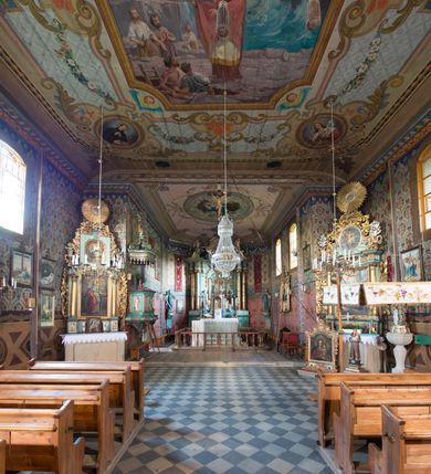 Zdjęcie nr 19: Kościół drewniany o konstrukcji zrębowej, na betonowym podmurowaniu przesłoniętym daszkiem, wieża o konstrukcji słupowej. Elewacje jednolite, szalowane w dolnej połowie pionowo, w górnej połowie poziomo, wzmocnione lisicami. Więźba dachowa drewniana, krokwiowa. Kościół orientowany, jednonawowy, nawa na rzucie prostokąta, prezbiterium nieco węższe, zakończone trójbocznie. Do wschodniej ściany prezbiterium przylega Ogrójec na rzucie prostokąta, od północy piętrowa zakrystia na planie prostokąta z niewielką prostokątną przybudówką od północy. Do zachodniej ściany nawy przylega wieża na planie kwadratu, do południowej ściany nawy kaplica na takim samym planie. 
Pomiędzy nawą a prezbiterium prostokątny otwór tęczowy. Wewnątrz ściany wzmocnione parami lizen, zakończone opasującym całość wnętrza profilowanym gzymsem. Parapet chóru muzycznego w zachodniej części nawy, o wypukłej środkowej części, podparty na czterech filarach. Zakrystia dwupiętrowa ze strychem, na drugim piętrze dawna loża kolatorska otwarta do wnętrza prezbiterium arkadą. Kaplica boczna dwupiętrowa, górne pomieszczenie dzielą od wnętrza dwa okna. Otwory drzwiowe o prostokątnym wykroju, zamknięte drzwiami spągowymi w południowej ścianie nawy oraz prezbiterium, drzwi w zachodniej ścianie dwuskrzydłowe. Wnętrze nakryte pułapami deskowymi o zaokrąglonych fasetach. Posadzka z płyt ceramicznych. 
Elewacja frontowa z dostawioną trójkondygnacyjną, zwężającą się ku górze wieżą, każda kondygnacja oddzielona daszkiem. Na osi oraz na południowej ścianie wejścia do kruchty w przyziemiu wieży z dwuskrzydłowymi drzwiami, frontowe nakryte dwuspadowym daszkiem z niszą na figurę Najświętszego Serca Jezusa. Prostokątne okna z dwóch stron pierwszej kondygnacji, trzech stron drugiej kondygnacji, w partii trzeciej z każdej strony para otworów dzwonnych. W elewacji północnej pięć otworów okiennych w formie stojącego prostokąta, dwa w nawie, po jednym w każdej kondygnacji zakrystii oraz w północnej przybudówce zakrystii wejście i małe prostokątne okienko. W elewacji południowej cztery okna w formie stojącego prostokąta, dwa w nawie i dwa w prezbiterium. W kaplicy bocznej okno i wejście w pierwszej kondygnacji oraz cztery okna w drugiej kondygnacji – dwa na ścianie frontowej oraz po jednym na bocznych. Na ścianie wschodniej prezbiterium Ogrójec w formie głębokiej szalowanej wnęki przesłoniętej dwuspadowym daszkiem. Kościół nakryty dachami dwuspadowymi z ceramicznej dachówki, wyższym nad nawą, niższym nad prezbiterium, nad zakrystią dach dwuspadowy, nad przybudówką pulpitowy. Kaplica przekryta blaszanym dachem dwuspadowym. Wieża zwieńczona hełmem baniastym pokrytym blachą, z ośmioboczną latarnią z otworami dzwonnymi, z pozorną izbicą. W połowie długości dachu nad nawą od strony prezbiterium wznosi się ponad kalenicą wieżyczka na sygnaturkę, na ośmiobocznym obitym blachą trzonie, z latarnią zwieńczoną niewielkim cebulastym, blaszanym hełmem zakończonym kulą z krzyżem. 