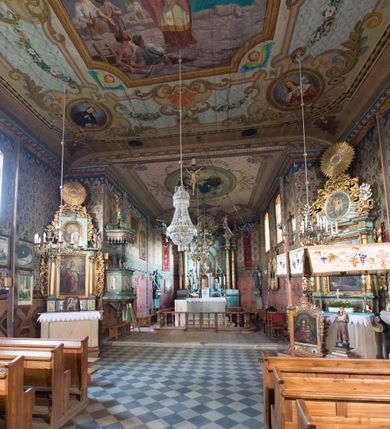 Zdjęcie nr 21: Kościół drewniany o konstrukcji zrębowej, na betonowym podmurowaniu przesłoniętym daszkiem, wieża o konstrukcji słupowej. Elewacje jednolite, szalowane w dolnej połowie pionowo, w górnej połowie poziomo, wzmocnione lisicami. Więźba dachowa drewniana, krokwiowa. Kościół orientowany, jednonawowy, nawa na rzucie prostokąta, prezbiterium nieco węższe, zakończone trójbocznie. Do wschodniej ściany prezbiterium przylega Ogrójec na rzucie prostokąta, od północy piętrowa zakrystia na planie prostokąta z niewielką prostokątną przybudówką od północy. Do zachodniej ściany nawy przylega wieża na planie kwadratu, do południowej ściany nawy kaplica na takim samym planie. 
Pomiędzy nawą a prezbiterium prostokątny otwór tęczowy. Wewnątrz ściany wzmocnione parami lizen, zakończone opasującym całość wnętrza profilowanym gzymsem. Parapet chóru muzycznego w zachodniej części nawy, o wypukłej środkowej części, podparty na czterech filarach. Zakrystia dwupiętrowa ze strychem, na drugim piętrze dawna loża kolatorska otwarta do wnętrza prezbiterium arkadą. Kaplica boczna dwupiętrowa, górne pomieszczenie dzielą od wnętrza dwa okna. Otwory drzwiowe o prostokątnym wykroju, zamknięte drzwiami spągowymi w południowej ścianie nawy oraz prezbiterium, drzwi w zachodniej ścianie dwuskrzydłowe. Wnętrze nakryte pułapami deskowymi o zaokrąglonych fasetach. Posadzka z płyt ceramicznych. 
Elewacja frontowa z dostawioną trójkondygnacyjną, zwężającą się ku górze wieżą, każda kondygnacja oddzielona daszkiem. Na osi oraz na południowej ścianie wejścia do kruchty w przyziemiu wieży z dwuskrzydłowymi drzwiami, frontowe nakryte dwuspadowym daszkiem z niszą na figurę Najświętszego Serca Jezusa. Prostokątne okna z dwóch stron pierwszej kondygnacji, trzech stron drugiej kondygnacji, w partii trzeciej z każdej strony para otworów dzwonnych. W elewacji północnej pięć otworów okiennych w formie stojącego prostokąta, dwa w nawie, po jednym w każdej kondygnacji zakrystii oraz w północnej przybudówce zakrystii wejście i małe prostokątne okienko. W elewacji południowej cztery okna w formie stojącego prostokąta, dwa w nawie i dwa w prezbiterium. W kaplicy bocznej okno i wejście w pierwszej kondygnacji oraz cztery okna w drugiej kondygnacji – dwa na ścianie frontowej oraz po jednym na bocznych. Na ścianie wschodniej prezbiterium Ogrójec w formie głębokiej szalowanej wnęki przesłoniętej dwuspadowym daszkiem. Kościół nakryty dachami dwuspadowymi z ceramicznej dachówki, wyższym nad nawą, niższym nad prezbiterium, nad zakrystią dach dwuspadowy, nad przybudówką pulpitowy. Kaplica przekryta blaszanym dachem dwuspadowym. Wieża zwieńczona hełmem baniastym pokrytym blachą, z ośmioboczną latarnią z otworami dzwonnymi, z pozorną izbicą. W połowie długości dachu nad nawą od strony prezbiterium wznosi się ponad kalenicą wieżyczka na sygnaturkę, na ośmiobocznym obitym blachą trzonie, z latarnią zwieńczoną niewielkim cebulastym, blaszanym hełmem zakończonym kulą z krzyżem. 