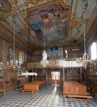 Zdjęcie nr 25: Kościół drewniany o konstrukcji zrębowej, na betonowym podmurowaniu przesłoniętym daszkiem, wieża o konstrukcji słupowej. Elewacje jednolite, szalowane w dolnej połowie pionowo, w górnej połowie poziomo, wzmocnione lisicami. Więźba dachowa drewniana, krokwiowa. Kościół orientowany, jednonawowy, nawa na rzucie prostokąta, prezbiterium nieco węższe, zakończone trójbocznie. Do wschodniej ściany prezbiterium przylega Ogrójec na rzucie prostokąta, od północy piętrowa zakrystia na planie prostokąta z niewielką prostokątną przybudówką od północy. Do zachodniej ściany nawy przylega wieża na planie kwadratu, do południowej ściany nawy kaplica na takim samym planie. 
Pomiędzy nawą a prezbiterium prostokątny otwór tęczowy. Wewnątrz ściany wzmocnione parami lizen, zakończone opasującym całość wnętrza profilowanym gzymsem. Parapet chóru muzycznego w zachodniej części nawy, o wypukłej środkowej części, podparty na czterech filarach. Zakrystia dwupiętrowa ze strychem, na drugim piętrze dawna loża kolatorska otwarta do wnętrza prezbiterium arkadą. Kaplica boczna dwupiętrowa, górne pomieszczenie dzielą od wnętrza dwa okna. Otwory drzwiowe o prostokątnym wykroju, zamknięte drzwiami spągowymi w południowej ścianie nawy oraz prezbiterium, drzwi w zachodniej ścianie dwuskrzydłowe. Wnętrze nakryte pułapami deskowymi o zaokrąglonych fasetach. Posadzka z płyt ceramicznych. 
Elewacja frontowa z dostawioną trójkondygnacyjną, zwężającą się ku górze wieżą, każda kondygnacja oddzielona daszkiem. Na osi oraz na południowej ścianie wejścia do kruchty w przyziemiu wieży z dwuskrzydłowymi drzwiami, frontowe nakryte dwuspadowym daszkiem z niszą na figurę Najświętszego Serca Jezusa. Prostokątne okna z dwóch stron pierwszej kondygnacji, trzech stron drugiej kondygnacji, w partii trzeciej z każdej strony para otworów dzwonnych. W elewacji północnej pięć otworów okiennych w formie stojącego prostokąta, dwa w nawie, po jednym w każdej kondygnacji zakrystii oraz w północnej przybudówce zakrystii wejście i małe prostokątne okienko. W elewacji południowej cztery okna w formie stojącego prostokąta, dwa w nawie i dwa w prezbiterium. W kaplicy bocznej okno i wejście w pierwszej kondygnacji oraz cztery okna w drugiej kondygnacji – dwa na ścianie frontowej oraz po jednym na bocznych. Na ścianie wschodniej prezbiterium Ogrójec w formie głębokiej szalowanej wnęki przesłoniętej dwuspadowym daszkiem. Kościół nakryty dachami dwuspadowymi z ceramicznej dachówki, wyższym nad nawą, niższym nad prezbiterium, nad zakrystią dach dwuspadowy, nad przybudówką pulpitowy. Kaplica przekryta blaszanym dachem dwuspadowym. Wieża zwieńczona hełmem baniastym pokrytym blachą, z ośmioboczną latarnią z otworami dzwonnymi, z pozorną izbicą. W połowie długości dachu nad nawą od strony prezbiterium wznosi się ponad kalenicą wieżyczka na sygnaturkę, na ośmiobocznym obitym blachą trzonie, z latarnią zwieńczoną niewielkim cebulastym, blaszanym hełmem zakończonym kulą z krzyżem. 