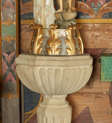 Zdjęcie nr 1: Wysoka podstawa na rzucie zbliżonym do kwadratu. Trzon tralkowy, kanelowany, ustawiony na kostce, zakończony profilowanym, ośmiobocznym pierścieniem. Czara półkolista, puklowana, o ośmiobocznym, profilowanym brzegu. Na boku podstawy inskrypcja: „A[nno] D[omini] 1728 KAS[…]”. Wewnątrz czary metalowa misa na wodę. Pokrywa drewniana, w formie cokołu, ujętego po bokach złoconymi liśćmi akantu, z drzwiczkami na froncie. Na niej ustawiona grupa rzeźbiarska Chrztu Chrystusa, z klęczącą frontalnie figurą Jezusa oraz stojącego obok, na skale św. Jana Chrzciciela, nad nimi Oko Opatrzności w glorii promienistej oraz gołębica Ducha Świętego. Na skale inskrypcje „966” i „1966”. 



