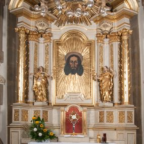 Zdjęcie nr 1: Ołtarz architektoniczny, przyścienny, jednoosiowy, jednokondygnacyjny z mensą. Mensa prosta, kamienna; antepedium płaskorzeźbione ze sceną Zesłania Ducha Świętego. Kompozycja jest niemal symetryczna, postacie apostołów oraz dwie Marie siedzą lub stoją poniżej rozchodzących się promieni glorii. Nastawa ołtarzowa ustawiona na wysokim, zdwojonym cokole, którego szersza oś środkowa jest flankowana parami cokołów ustawionych skośnie. Pierwsza kondygnacja również ustawiona na cokole, którego pola wypełniają płyciny z płaskorzeźbioną, symetryczną dekoracją z ceownicami wokół kwiatu róży. Na środku, na mensie prostopadłościenne tabernakulum na cokole. Na jego ścianie frontowej wypełnione czerwonym kolorem drzwi w kształcie stojącego prostokąta zamkniętego od góry łukiem nadwieszonym, flankowane kolumienkami jońskimi. 
W polu środkowym pierwszej kondygnacji ołtarza obraz „Oblicze Chrystusa” (XVII w.) w profilowanej, prostokątnej ramie z uskokiem i półkolistym zamknięciem od góry. Pole flankowane skośnie ustawionymi kolumnami korynckimi na tle pilastrów, wspierającymi wyłamane nad nimi belkowanie i fragmenty przerwanego przyczółka. Trzony kolumn ozdobione plastycznymi płomieniami. Na pilastrach płyciny z wypełnieniem z płaskorzeźbionych ornamentów o motywach regencyjnych. Na tle pilastrów, po obu stronach środkowego obrazu, rzeźbione figury św. Heleny i św. Barbary w obficie drapowanych szatach. 
Zwieńczenie ołtarza w formie glorii promienistej z gołębicą Ducha Świętego pośrodku. Poniżej niej, na banderoli inskrypcja „EMITTE  SPIRITUM TUUM ET CREABUNTUR”. Przedstawienie ujęte otokiem utworzonym z obłoków i uskrzydlonych główek. Po bokach, na częściach przerwanego belkowania, na obłokach siedzą putta. Są zwrócone do siebie i spoglądają lekko w dół. Mają uniesione ręce i są przepasane złotymi szarfami. 
Struktura ołtarza dekorowana imitacją marmoryzacji za pomocą polichromii na kolor jasnoszary z ciemniejszymi żyłkami; profile, ornamenty, gloria, szaty świętych złocone; obłoki, gołębica, elementy strojów, fragmenty antepedium srebrzone; polichromia w partiach ciała postaci naturalistyczna. 