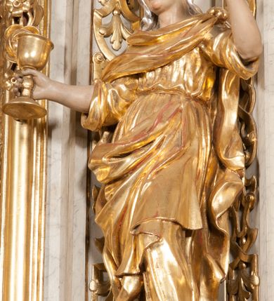 Zdjęcie nr 2: Figura pełna, na cokole, przedstawiająca św. Barbarę. Święta w pozie przypominającej literę „S”, w kontrapoście z ciężarem na prawej nodze, z lewą odstawioną do boku. Obie ręce zgięte w łokciach, w prawej trzyma kielich, lewą unosi do góry w delikatnym geście. Głowa przechylona na prawo, twarz o łagodnym wyrazie, okrągła, z wysokim czołem, małymi, przymkniętymi oczami, niewielkim nosem i wąskimi ustami; brązowe włosy zaczesane do tyłu, okryte chustką. Święta jest ubrana w długą, przepasaną suknię, która podkreśla kształt ciała, przylegając do niego drobnymi fałdami; rękawy sukni szerokie, sięgające łokci. Barbara na suknię ma zarzucony płaszcz, który przykrywa dekolt, owija się wokół prawej ręki i jest podczepiony do paska na lewym biodrze. 
Polichromia w partiach ciała naturalistyczna, szaty i atrybut złocone, chustka srebrzona. 