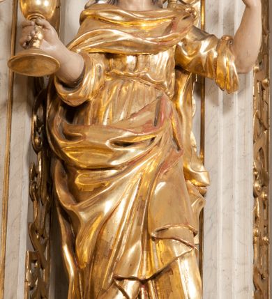 Zdjęcie nr 1: Figura pełna, na cokole, przedstawiająca św. Barbarę. Święta w pozie przypominającej literę „S”, w kontrapoście z ciężarem na prawej nodze, z lewą odstawioną do boku. Obie ręce zgięte w łokciach, w prawej trzyma kielich, lewą unosi do góry w delikatnym geście. Głowa przechylona na prawo, twarz o łagodnym wyrazie, okrągła, z wysokim czołem, małymi, przymkniętymi oczami, niewielkim nosem i wąskimi ustami; brązowe włosy zaczesane do tyłu, okryte chustką. Święta jest ubrana w długą, przepasaną suknię, która podkreśla kształt ciała, przylegając do niego drobnymi fałdami; rękawy sukni szerokie, sięgające łokci. Barbara na suknię ma zarzucony płaszcz, który przykrywa dekolt, owija się wokół prawej ręki i jest podczepiony do paska na lewym biodrze. 
Polichromia w partiach ciała naturalistyczna, szaty i atrybut złocone, chustka srebrzona. 