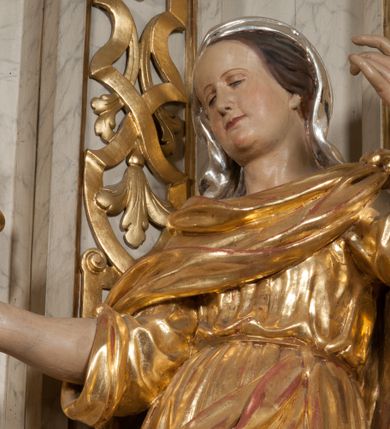 Zdjęcie nr 5: Figura pełna, na cokole, przedstawiająca św. Barbarę. Święta w pozie przypominającej literę „S”, w kontrapoście z ciężarem na prawej nodze, z lewą odstawioną do boku. Obie ręce zgięte w łokciach, w prawej trzyma kielich, lewą unosi do góry w delikatnym geście. Głowa przechylona na prawo, twarz o łagodnym wyrazie, okrągła, z wysokim czołem, małymi, przymkniętymi oczami, niewielkim nosem i wąskimi ustami; brązowe włosy zaczesane do tyłu, okryte chustką. Święta jest ubrana w długą, przepasaną suknię, która podkreśla kształt ciała, przylegając do niego drobnymi fałdami; rękawy sukni szerokie, sięgające łokci. Barbara na suknię ma zarzucony płaszcz, który przykrywa dekolt, owija się wokół prawej ręki i jest podczepiony do paska na lewym biodrze. 
Polichromia w partiach ciała naturalistyczna, szaty i atrybut złocone, chustka srebrzona. 