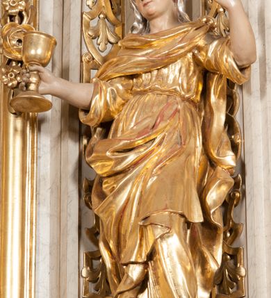 Zdjęcie nr 3: Figura pełna, na cokole, przedstawiająca św. Barbarę. Święta w pozie przypominającej literę „S”, w kontrapoście z ciężarem na prawej nodze, z lewą odstawioną do boku. Obie ręce zgięte w łokciach, w prawej trzyma kielich, lewą unosi do góry w delikatnym geście. Głowa przechylona na prawo, twarz o łagodnym wyrazie, okrągła, z wysokim czołem, małymi, przymkniętymi oczami, niewielkim nosem i wąskimi ustami; brązowe włosy zaczesane do tyłu, okryte chustką. Święta jest ubrana w długą, przepasaną suknię, która podkreśla kształt ciała, przylegając do niego drobnymi fałdami; rękawy sukni szerokie, sięgające łokci. Barbara na suknię ma zarzucony płaszcz, który przykrywa dekolt, owija się wokół prawej ręki i jest podczepiony do paska na lewym biodrze. 
Polichromia w partiach ciała naturalistyczna, szaty i atrybut złocone, chustka srebrzona. 