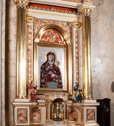 Zdjęcie nr 3: Ołtarz architektoniczny, przyścienny, jednokondygnacyjny, jednoosiowy, w formie aediculi, ustawiony na wysokim cokole. Do niego przystawiona prostopadłościenna mensa, z antepedium ozdobionym trzema płycinami: zewnętrze mają kształt kwadratu i są wypełnione polichromią imitującą marmoryzację, środkowa, w kształcie leżącego prostokąta, ozdobiona jest monogramem maryjnym. Na mensie tabernakulum z tronem do wystawiania, na rzucie zbliżonym do owalu. Ustawione na wysokim cokole, w którym prostokątne drzwiczki. Tron do wystawiania w formie dekorowanej kotarą niszy wypełnionej grupą Ukrzyżowania z Marią i św. Janem, utrzymanej w stylistyce ludowej. Na cokole przedstawiono narzędzia murarskie oraz Serce Jezusa. Niszę flankują pary kolumn, całość wieńczy silnie profilowane belkowanie.  
Nastawa ołtarzowa na własnym cokole z wyodrębnionymi po bokach prostopadłościennymi postumentami pod znajdujące się wyżej kolumny, dekorowanymi od przodu prostokątnymi płycinami; inne powierzchnie partii cokołowej ołtarza (m.in. po bokach tabernakulum) ożywione prostokątnymi, zestawionymi względem siebie w symetryczne pary płycinami, każda ze ściętym jednym z górnych narożników. W polu centralnym środkowej partii retabulum rama w kształcie pionowego prostokąta zamkniętego od góry łukiem wklęsło-wypukłym z uskokiem. W niej obraz z przedstawieniem Matki Boskiej w typie Śnieżnej trzymającej szkaplerz, wyobrażonej poniżej monogramu maryjnego uwitego ze złotej wstęgi. Pole flankowane pilastrami jońskimi, przed którymi ustawione kolumny o kapitelach utworzonych z kimationów, podtrzymujące pełne belkowanie przełamujące się na ich osi. Fryz belkowania dekorowany kolistymi medalionami z głowami aniołków i głową Chrystusa na środku. Przy podstawach kolumn dwie figury ewangelistów. Ponad belkowaniem rozsunięte fragmenty przerwanego, trójkątnego przyczółka. Na belkowaniu, w centrum figura św. Józefa z Dzieciątkiem na lewym ramieniu i lilią w prawej ręce. W zwieńczeniu na osi kolumn figurki siedzących aniołków, trzymających narzędzia murarskie. 
Trzony pilastrów dekorowane kampanulami, ich głowice girlandami kwiatów oraz muszlami; w tle pola głównej kondygnacji gałązki kwiatowe; gzyms tamże w formie fryzu palmetowego, kolejny na mensie.  
Struktura w kolorze kremowym lub pokryta imitacją marmoryzacji w kolorze różowym; niektóre pola malowane na kolor ciemnopomarańczowy; kolumny, profile, ornamenty złocone; elementy figur, medalionów oraz głowic złocone i srebrzone.