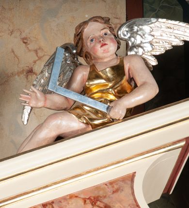 Zdjęcie nr 29: Ołtarz architektoniczny, przyścienny, jednokondygnacyjny, jednoosiowy, w formie aediculi, ustawiony na wysokim cokole. Do niego przystawiona prostopadłościenna mensa, z antepedium ozdobionym trzema płycinami: zewnętrze mają kształt kwadratu i są wypełnione polichromią imitującą marmoryzację, środkowa, w kształcie leżącego prostokąta, ozdobiona jest monogramem maryjnym. Na mensie tabernakulum z tronem do wystawiania, na rzucie zbliżonym do owalu. Ustawione na wysokim cokole, w którym prostokątne drzwiczki. Tron do wystawiania w formie dekorowanej kotarą niszy wypełnionej grupą Ukrzyżowania z Marią i św. Janem, utrzymanej w stylistyce ludowej. Na cokole przedstawiono narzędzia murarskie oraz Serce Jezusa. Niszę flankują pary kolumn, całość wieńczy silnie profilowane belkowanie.  
Nastawa ołtarzowa na własnym cokole z wyodrębnionymi po bokach prostopadłościennymi postumentami pod znajdujące się wyżej kolumny, dekorowanymi od przodu prostokątnymi płycinami; inne powierzchnie partii cokołowej ołtarza (m.in. po bokach tabernakulum) ożywione prostokątnymi, zestawionymi względem siebie w symetryczne pary płycinami, każda ze ściętym jednym z górnych narożników. W polu centralnym środkowej partii retabulum rama w kształcie pionowego prostokąta zamkniętego od góry łukiem wklęsło-wypukłym z uskokiem. W niej obraz z przedstawieniem Matki Boskiej w typie Śnieżnej trzymającej szkaplerz, wyobrażonej poniżej monogramu maryjnego uwitego ze złotej wstęgi. Pole flankowane pilastrami jońskimi, przed którymi ustawione kolumny o kapitelach utworzonych z kimationów, podtrzymujące pełne belkowanie przełamujące się na ich osi. Fryz belkowania dekorowany kolistymi medalionami z głowami aniołków i głową Chrystusa na środku. Przy podstawach kolumn dwie figury ewangelistów. Ponad belkowaniem rozsunięte fragmenty przerwanego, trójkątnego przyczółka. Na belkowaniu, w centrum figura św. Józefa z Dzieciątkiem na lewym ramieniu i lilią w prawej ręce. W zwieńczeniu na osi kolumn figurki siedzących aniołków, trzymających narzędzia murarskie. 
Trzony pilastrów dekorowane kampanulami, ich głowice girlandami kwiatów oraz muszlami; w tle pola głównej kondygnacji gałązki kwiatowe; gzyms tamże w formie fryzu palmetowego, kolejny na mensie.  
Struktura w kolorze kremowym lub pokryta imitacją marmoryzacji w kolorze różowym; niektóre pola malowane na kolor ciemnopomarańczowy; kolumny, profile, ornamenty złocone; elementy figur, medalionów oraz głowic złocone i srebrzone.