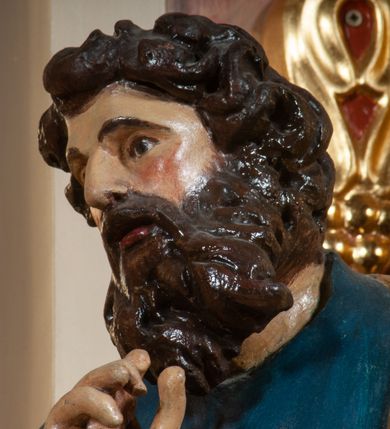 Zdjęcie nr 3: Figura pełna na cokole. Ewangelista ukazany w całej postaci, stojący frontalnie (choć przesunięcie cokołu powoduje, że postać sprawia wrażenie skierowanej w bok), w kontrapoście, z lewą nogą zgiętą w kolanie, jej stopą odsuniętą do tyłu, opartą na palcach. Prawą rękę święty unosi do góry na wysokość piersi, lewą, zgiętą w łokciu podtrzymuje otwartą, ułożoną poziomo księgę; patrzy przed siebie. Ma owalną twarz o okrągłych, szeroko otwartych oczach, ponad którymi widoczne uniesione brwi, o prostym nosie i szerokich ustach; na policzkach rumieńce. Włosy zwinięte w pukle zasłaniają uszy, grube wąsy i jakby rozwiana broda okalają twarz. Ewangelista jest ubrany w niebieską suknię, która grubymi fałdami marszczy się na rękawach, a w części głównej równoległymi fałdami opada w dół, zawijając się nieznacznie w lewą stronę na wysokości kostek. Skośnie przez przód i plecy ma zarzucony złoty płaszcz. Włosy i zarost brązowe, polichromia w odsłoniętych partiach karnacji traktowana naturalistycznie.