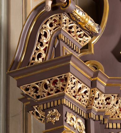 Zdjęcie nr 7: Ołtarz przyścienny, architektoniczny, jednoosiowy, jednokondygnacjowy ze zwieńczeniem. Retabulum ustawione na wysokim cokole, przed którym stoi mensa w typie sarkofagowym. Na mensie tabernakulum w formie prostopadłościanu, którego ściana frontowa jest flankowana parą dostawionych skośnie kolumn, a tylna wolutami. Tabernakulum na cokole, na ścianie frontowej drzwi w kształcie prostokąta zamkniętego od góry łukiem nadwieszonym, z przedstawieniem wypukłorzeźbionej, silnie plastycznej sceny chrztu Chrystusa. Z prawej strony św. Jan Chrzciciel, który prawym kolanem klęczy na głazie, prawą ręką polewa wodą głowę stojącego po lewej stronie Chrystusa. Za nimi dwie postaci, powyżej gołębica Ducha Świętego. W górnych narożnikach ściany frontowej tabernakulum dwa, symetrycznie ułożone ornamenty rocaille. Główne pole właściwego retabulum flankują kolumny korynckie o trzonach dekorowanych wicią, ustawione na tle zwielokrotnionych pilastrów; podpory posadowione na ukośnie ustawionych, rozsuniętych postumentach dekorowanych kwadratowymi płycinami, dźwigają  belkowanie przełamane na ich osiach, z odcinkami także ustawionymi skośnie. W prostokątnym polu głównym nastawy ołtarzowej obraz z przedstawieniem Matki Boskiej Bolesnej poniżej monogramu maryjnego uwitego ze wstęgi, w prostokątnej ramie zamkniętej od góry łukiem nadwieszonym. Górne naroża pola wypełniają płomieniste motywy rocaille przechodzące w dół w fantazyjną wić roślinną.  Na fryzie belkowania umieszczono ornament roślinny z muszlami, a dolna część gzymsu ma formę pasa ażurowej dekoracji z motywów rocaille na czerwonym tle. Na środku tej dekoracji niewielki kartusz z napisem. Na rozsuniętych odcinkach belkowania, na osi kolumn, umieszczone fragmenty pękniętego półkolistego przyczółka; na nich siedzą anioły. Zwieńczenie umieszczone pomiędzy tymi odcinkami w formie ścianki o ogólnym zarysie trapezu o wklęsłych bokach. Wypełnia ją obraz z przedstawieniem św. Antoniego we wklęsło-wypukłej ramie powtarzającej zarys zwieńczenia, które od góry zamknięte jest dwoma wolutami. W miejscu ich styku, na osi, rzeźbione przedstawienie tronującego Boga Ojca pośród chmur, powyżej główek anielskich i na tle glorii promienistej. Bóg prawą rękę wznosi do góry, lewą trzyma na jabłku królewskim i przytrzymuje berło, u stóp gołębica Ducha Świętego. Struktura ołtarza malowana na kolor brązowy; profile, detale, ornamenty i kolumny złocone, postacie w partiach karnacji  polichromowane naturalistycznie.