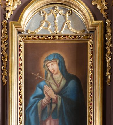 Zdjęcie nr 3: Ołtarz przyścienny, architektoniczny, jednoosiowy, jednokondygnacjowy ze zwieńczeniem. Retabulum ustawione na wysokim cokole, przed którym stoi mensa w typie sarkofagowym. Na mensie tabernakulum w formie prostopadłościanu, którego ściana frontowa jest flankowana parą dostawionych skośnie kolumn, a tylna wolutami. Tabernakulum na cokole, na ścianie frontowej drzwi w kształcie prostokąta zamkniętego od góry łukiem nadwieszonym, z przedstawieniem wypukłorzeźbionej, silnie plastycznej sceny chrztu Chrystusa. Z prawej strony św. Jan Chrzciciel, który prawym kolanem klęczy na głazie, prawą ręką polewa wodą głowę stojącego po lewej stronie Chrystusa. Za nimi dwie postaci, powyżej gołębica Ducha Świętego. W górnych narożnikach ściany frontowej tabernakulum dwa, symetrycznie ułożone ornamenty rocaille. Główne pole właściwego retabulum flankują kolumny korynckie o trzonach dekorowanych wicią, ustawione na tle zwielokrotnionych pilastrów; podpory posadowione na ukośnie ustawionych, rozsuniętych postumentach dekorowanych kwadratowymi płycinami, dźwigają  belkowanie przełamane na ich osiach, z odcinkami także ustawionymi skośnie. W prostokątnym polu głównym nastawy ołtarzowej obraz z przedstawieniem Matki Boskiej Bolesnej poniżej monogramu maryjnego uwitego ze wstęgi, w prostokątnej ramie zamkniętej od góry łukiem nadwieszonym. Górne naroża pola wypełniają płomieniste motywy rocaille przechodzące w dół w fantazyjną wić roślinną.  Na fryzie belkowania umieszczono ornament roślinny z muszlami, a dolna część gzymsu ma formę pasa ażurowej dekoracji z motywów rocaille na czerwonym tle. Na środku tej dekoracji niewielki kartusz z napisem. Na rozsuniętych odcinkach belkowania, na osi kolumn, umieszczone fragmenty pękniętego półkolistego przyczółka; na nich siedzą anioły. Zwieńczenie umieszczone pomiędzy tymi odcinkami w formie ścianki o ogólnym zarysie trapezu o wklęsłych bokach. Wypełnia ją obraz z przedstawieniem św. Antoniego we wklęsło-wypukłej ramie powtarzającej zarys zwieńczenia, które od góry zamknięte jest dwoma wolutami. W miejscu ich styku, na osi, rzeźbione przedstawienie tronującego Boga Ojca pośród chmur, powyżej główek anielskich i na tle glorii promienistej. Bóg prawą rękę wznosi do góry, lewą trzyma na jabłku królewskim i przytrzymuje berło, u stóp gołębica Ducha Świętego. Struktura ołtarza malowana na kolor brązowy; profile, detale, ornamenty i kolumny złocone, postacie w partiach karnacji  polichromowane naturalistycznie.