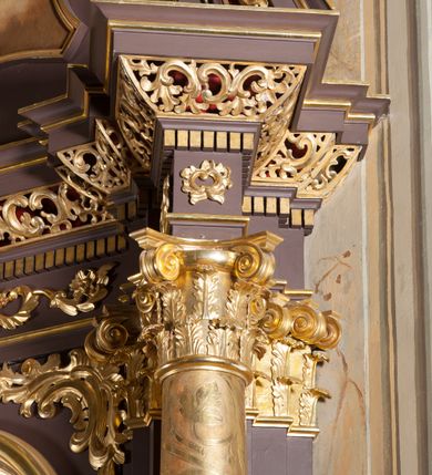 Zdjęcie nr 10: Ołtarz przyścienny, architektoniczny, jednoosiowy, jednokondygnacjowy ze zwieńczeniem. Retabulum ustawione na wysokim cokole, przed którym stoi mensa w typie sarkofagowym. Na mensie tabernakulum w formie prostopadłościanu, którego ściana frontowa jest flankowana parą dostawionych skośnie kolumn, a tylna wolutami. Tabernakulum na cokole, na ścianie frontowej drzwi w kształcie prostokąta zamkniętego od góry łukiem nadwieszonym, z przedstawieniem wypukłorzeźbionej, silnie plastycznej sceny chrztu Chrystusa. Z prawej strony św. Jan Chrzciciel, który prawym kolanem klęczy na głazie, prawą ręką polewa wodą głowę stojącego po lewej stronie Chrystusa. Za nimi dwie postaci, powyżej gołębica Ducha Świętego. W górnych narożnikach ściany frontowej tabernakulum dwa, symetrycznie ułożone ornamenty rocaille. Główne pole właściwego retabulum flankują kolumny korynckie o trzonach dekorowanych wicią, ustawione na tle zwielokrotnionych pilastrów; podpory posadowione na ukośnie ustawionych, rozsuniętych postumentach dekorowanych kwadratowymi płycinami, dźwigają  belkowanie przełamane na ich osiach, z odcinkami także ustawionymi skośnie. W prostokątnym polu głównym nastawy ołtarzowej obraz z przedstawieniem Matki Boskiej Bolesnej poniżej monogramu maryjnego uwitego ze wstęgi, w prostokątnej ramie zamkniętej od góry łukiem nadwieszonym. Górne naroża pola wypełniają płomieniste motywy rocaille przechodzące w dół w fantazyjną wić roślinną.  Na fryzie belkowania umieszczono ornament roślinny z muszlami, a dolna część gzymsu ma formę pasa ażurowej dekoracji z motywów rocaille na czerwonym tle. Na środku tej dekoracji niewielki kartusz z napisem. Na rozsuniętych odcinkach belkowania, na osi kolumn, umieszczone fragmenty pękniętego półkolistego przyczółka; na nich siedzą anioły. Zwieńczenie umieszczone pomiędzy tymi odcinkami w formie ścianki o ogólnym zarysie trapezu o wklęsłych bokach. Wypełnia ją obraz z przedstawieniem św. Antoniego we wklęsło-wypukłej ramie powtarzającej zarys zwieńczenia, które od góry zamknięte jest dwoma wolutami. W miejscu ich styku, na osi, rzeźbione przedstawienie tronującego Boga Ojca pośród chmur, powyżej główek anielskich i na tle glorii promienistej. Bóg prawą rękę wznosi do góry, lewą trzyma na jabłku królewskim i przytrzymuje berło, u stóp gołębica Ducha Świętego. Struktura ołtarza malowana na kolor brązowy; profile, detale, ornamenty i kolumny złocone, postacie w partiach karnacji  polichromowane naturalistycznie.