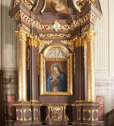 Zdjęcie nr 3: Obraz w kształcie zbliżonym do trapezu o krawędziach bocznych lekko wklęsłych, a dolnej i górnej wklęsło-wypukłej. Obraz przedstawia wizję św. Antoniego. Święty usytuowany nieco na lewo od osi kompozycji, zwrócony w trzech czwartych w lewo, klęczy na ziemi, ręce  założone ma przed sobą na wysokości klatki piersiowej i patrzy na ukazujące mu się Dzieciątko. Antoni ma małą głowę z dużymi oczami, nosem i cofniętym podbródkiem. Krótkie, brązowe włosy przysłaniają ucho, na brodzie krótki zarost. Ubrany w brązowy, obszerny habit z kapturem, łamiący się w grube fałdy. Przed nim, po prawej stronie obrazu u góry Dzieciątko. Chrystus unosi się ponad otwartą księgą i złożonym na niej kwiatem lilii. Prawą nogę wyciąga do przodu, lewą, zgiętą w kolanie ma cofniętą, prawą rękę wyciąga w stronę św. Antoniego w geście błogosławieństwa, lewą podtrzymuje białą tkaninę, która przechodzi przez obie ręce, zasłania przód ciała i regularnymi fałdami opada wzdłuż lewej nogi. Tło wypełniają jasnożółte obłoki na tle ciemniejszego nieba, u góry dwie główki anielskie. Obraz w złoconej, profilowanej ramie.