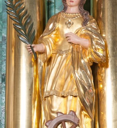 Zdjęcie nr 12: Nastawa ołtarzowa architektoniczna, jednokondygnacyjna, trójosiowa ze zwieńczeniem. 
Mensa w typie sarkofagowym, na niej rozbudowane, architektoniczne, dwukondygnacyjne, trójosiowe tabernakulum o wklęsło-wypukłej strukturze. Dolną kondygnację tabernakulum stanowi dwudzielny cokół przerwany w części środkowej na szafkę zamykaną drzwiczkami zdobionymi symbolami eucharystycznymi. Drugą kondygnację stanowi tron wystawienia – półkolista wnęka zdobiona motywem kiści winogron, z gołębicą Ducha Świętego na podniebieniu. Tron jest flankowany wnękami z dekoracją rocaille&#039;ową oraz parami kolumn na tle pilastrów. Na dźwiganym przez kolumny rozbudowanym belkowaniu przeciwstawnie ustawione anioły kierują swój wzrok na krucyfiks. Zwieńczenie osi centralnej stanowi posążek baranka stojącego na księdze z siedmioma pieczęciami. 
Nastawa ołtarzowa jest oparta na wysokim, dwudzielnym cokole. Pole środkowe wypełnia nisza w kształcie stojącego prostokąta zamkniętego półkoliście z umieszczonym w niej obrazem Serca Pana Jezusa, powyżej którego znajduje się utworzony z motywów płomienistych rocaille&#039;ów kartusz z koroną umieszczoną ponad dwoma skrzyżowanymi berłami. Pole centralne flankowane parami kolumn o rozbudowanych, kompozytowych kapitelach złożonych ze stylizowanych liści akantu i palmety pomiędzy wolutami, stojącymi na tle pilastrów połączonych fryzem palmetowym. Między nimi figury świętych: Katarzyny po lewej stronie i Barbary po prawej. Nastawa ujęta uszami z rocaille&#039;u i spływów wolutowych. Kolumny dźwigają wyłamane na ich osiach belkowanie dekorowane kimationem i ząbkowaniem, z przyczółkiem przerwanym na rozbudowaną kompozycję Trójcy Świętej. W centrum przedstawienia siedzą Chrystus trzymający obiema rękami krzyż łaciński oraz Bóg Ojciec błogosławiący prawą i trzymający berło w lewej ręce. Między nimi drugi symbol władzy królewskiej – jabłko zwieńczone krzyżem, stanowiące również odniesiecie do globu ziemskiego. Postacie tronują wśród chmur, w których umieszczono główki aniołków. Powyżej nich gołębica Ducha Świętego w centrum glorii promienistej stanowiącej tło dla przedstawienia.  
 Struktura marmoryzowana na kolor zielony i niebieski; kolumny, detale, figury oraz tabernakulum złocone i srebrzone, polichromia figur w partiach ciała naturalistyczna.
