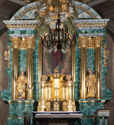 Zdjęcie nr 2: Nastawa ołtarzowa architektoniczna, jednokondygnacyjna, trójosiowa ze zwieńczeniem. 
Mensa w typie sarkofagowym, na niej rozbudowane, architektoniczne, dwukondygnacyjne, trójosiowe tabernakulum o wklęsło-wypukłej strukturze. Dolną kondygnację tabernakulum stanowi dwudzielny cokół przerwany w części środkowej na szafkę zamykaną drzwiczkami zdobionymi symbolami eucharystycznymi. Drugą kondygnację stanowi tron wystawienia – półkolista wnęka zdobiona motywem kiści winogron, z gołębicą Ducha Świętego na podniebieniu. Tron jest flankowany wnękami z dekoracją rocaille'ową oraz parami kolumn na tle pilastrów. Na dźwiganym przez kolumny rozbudowanym belkowaniu przeciwstawnie ustawione anioły kierują swój wzrok na krucyfiks. Zwieńczenie osi centralnej stanowi posążek baranka stojącego na księdze z siedmioma pieczęciami. 
Nastawa ołtarzowa jest oparta na wysokim, dwudzielnym cokole. Pole środkowe wypełnia nisza w kształcie stojącego prostokąta zamkniętego półkoliście z umieszczonym w niej obrazem Serca Pana Jezusa, powyżej którego znajduje się utworzony z motywów płomienistych rocaille'ów kartusz z koroną umieszczoną ponad dwoma skrzyżowanymi berłami. Pole centralne flankowane parami kolumn o rozbudowanych, kompozytowych kapitelach złożonych ze stylizowanych liści akantu i palmety pomiędzy wolutami, stojącymi na tle pilastrów połączonych fryzem palmetowym. Między nimi figury świętych: Katarzyny po lewej stronie i Barbary po prawej. Nastawa ujęta uszami z rocaille'u i spływów wolutowych. Kolumny dźwigają wyłamane na ich osiach belkowanie dekorowane kimationem i ząbkowaniem, z przyczółkiem przerwanym na rozbudowaną kompozycję Trójcy Świętej. W centrum przedstawienia siedzą Chrystus trzymający obiema rękami krzyż łaciński oraz Bóg Ojciec błogosławiący prawą i trzymający berło w lewej ręce. Między nimi drugi symbol władzy królewskiej – jabłko zwieńczone krzyżem, stanowiące również odniesiecie do globu ziemskiego. Postacie tronują wśród chmur, w których umieszczono główki aniołków. Powyżej nich gołębica Ducha Świętego w centrum glorii promienistej stanowiącej tło dla przedstawienia.  
 Struktura marmoryzowana na kolor zielony i niebieski; kolumny, detale, figury oraz tabernakulum złocone i srebrzone, polichromia figur w partiach ciała naturalistyczna.
