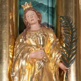 Zdjęcie nr 1: Rzeźba pełna, postać umieszczona na cokole; święta ustawiona  frontalnie, z głową przechyloną na prawe ramię. W lewej ręce trzyma palmę męczeńską, prawą przytrzymuje kielich chwycony przez płaszcz. Twarz owalna, bez wyrazu, oczy małe, nos prosty, usta niewielkie. Falowane, brązowe włosy spływają jej na plecy, jeden pukiel przechodzi do przodu; na głowie korona. Święta jest ubrana w bogato fałdowaną suknię z szeroką bordiurą pod szyją i dekoracją z ornamentów roślinnych na dekolcie. Okrywający suknię płaszcz przechodzi przez plecy i jest przerzucony przez obie ręce. Widoczne wysuwające się spod szat końce brązowych butów. 
Szaty, korona i kielich złocone; w partiach ciała polichromia naturalistyczna; gałązka palmy zielona. 
