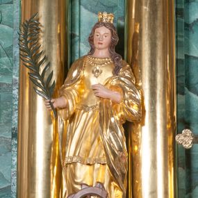 Zdjęcie nr 1: Rzeźba pełna, postać umieszczona na cokole; święta ustawiona w kontrapoście, z lewą nogą wysuniętą do przodu. W prawej dłoni trzyma palmę męczeńską, lewą ugiętą podtrzymuje fałdy płaszcza. Twarz owalna, bez wyrazu, oczy małe, nos prosty, niewielkie usta; falowane, brązowe włosy spływają na plecy, jeden pukiel przechodzi do przodu; na głowie korona. Święta jest ubrana w bogato fałdowaną suknię z gorsetem podkreślającą kształt ciała. Pod szyją ma dwa sznury korali, na jednym zawieszony medalion. Okrywający suknię płaszcz zarzucony na ramiona i plecy opada do ziemi, jedna część przerzucona przez lewą rękę. Spod sukni wystają fragmenty brązowych butów. U dołu, przed świętą połamane koło. 
Szaty i korona złocone, w partiach ciała polichromia naturalistyczna, liść palmy zielony, koło brązowe.