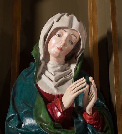 Zdjęcie nr 4: Rzeźba pełna, na cokole. Maria przedstawiona w całej postaci, w pozycji stojącej w ujęciu frontalnym. Ręce składa do modlitwy, głowę ma pochyloną na lewe ramię, spogląda w dół. Na jej łagodnej twarzy maluje się smutek, spod uniesionych brwi spoglądają duże, szare oczy o zewnętrznych kącikach skierowany w dół, nos mały, usta drobne, czerwone; na policzkach rumieńce. 
Maria jest ubrana w długą, czerwoną suknię. Głowę okrywa  biały welon, a dekolt tego samego koloru podwika. Na suknię ma narzucony niebieski płaszcz z zielonym podbiciem, który układa się w gęste, głębokie fałdy i wywija w formę kołnierza, wokół dłoni oraz tworzy małą rozetkę przy prawej stopie. Spod sukni wystają szpiczaste pantofelki. Polichromia w partiach ciała naturalistyczna. 
