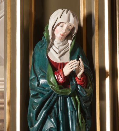 Zdjęcie nr 1: Rzeźba pełna, na cokole. Maria przedstawiona w całej postaci, w pozycji stojącej w ujęciu frontalnym. Ręce składa do modlitwy, głowę ma pochyloną na lewe ramię, spogląda w dół. Na jej łagodnej twarzy maluje się smutek, spod uniesionych brwi spoglądają duże, szare oczy o zewnętrznych kącikach skierowany w dół, nos mały, usta drobne, czerwone; na policzkach rumieńce. 
Maria jest ubrana w długą, czerwoną suknię. Głowę okrywa  biały welon, a dekolt tego samego koloru podwika. Na suknię ma narzucony niebieski płaszcz z zielonym podbiciem, który układa się w gęste, głębokie fałdy i wywija w formę kołnierza, wokół dłoni oraz tworzy małą rozetkę przy prawej stopie. Spod sukni wystają szpiczaste pantofelki. Polichromia w partiach ciała naturalistyczna. 
