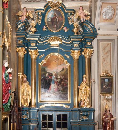 Zdjęcie nr 2: Ołtarz przyścienny, architektoniczny, jednoosiowy, jednokondygnacjowy ze zwieńczeniem. Retabulum ustawione na wysokim, dwukondygnacjowym  cokole o wyższej kondygnacji dolnej, z dwoma postumentami wyodrębnionymi po bokach;  powierzchnia cokołu dekorowana płycinami w kształcie prostokątów. Cokół przerwany w środku drzwiami do zakrystii ze skrzydłami w formie pionowych prostokątów podzielonych – każde skrzydło – na osiem mniejszych pól. Pole centralne ołtarza wypełnia obraz z przedstawieniem św. Kingi  odkrywającej złoża soli. Obraz ujęty w ramę w kształcie pionowego prostokąta zamkniętego łukiem wklęsło-wypukłym z uskokami; poniżej wstęga z inskrypcją „S(ANCTA) CUNEGUNDA ORA PRO NOBIS”. Pole z obrazem flankowane jest parami kolumn korynckich, z których zewnętrzne są wysunięte do przodu. Przed nie występują do przodu konsole na których ustawiono rzeźby św. Wojciecha i św. Stanisława. Kolumny dźwigają belkowanie przełamane na ich osiach i wygięte ku górze na linii płytkiego łuku odcinkowego powyżej obrazu;  pośrodku łuku dekoracja w formie dużej muszli. Na fryzie przełamanych fragmentów belkowania plakiety utworzone z dekoracji roślinnej; na osiach wewnętrznych kolumn, ponad belkowaniem, wazony z kwiatami. Ponad kolumnami zewnętrznymi i belkowaniem widoczne rozsunięte odcinki półkolistego, pękniętego przyczółka, na których posadowiono figurki aniołków. Pomiędzy odcinkami przyczółka zwieńczenie o formie ścianki w ogólnym kształcie zbliżonej do trapezu, o wklęsłych bokach zakończonych u dołu wolutami,  zamkniętej łukiem nadwieszonym; ścianka od góry zwieńczona częściowo niepełnym belkowaniem. Owalne pole pośrodku zwieńczenia wypełnia obraz z przedstawieniem św. Floriana; po bokach ramy rozmieszczone główki anielskie i plakiety z dekoracją roślinną. Ponad obrazem, na tle gzymsu belkowania od góry zamykającego zwieńczenie, widoczny medalion z monogramem Chrystusa otoczony obłokami, na tle glorii promienistej.  
Struktura retabulum malowana na kolor niebieski; profile, kolumny, ornamenty, detale złocone; figury oraz gloria złocone i srebrzone.
