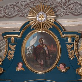 Zdjęcie nr 1: Obraz w kształcie stojącego owalu z przedstawieniem św. Floriana. W centrum kompozycji święty przedstawiony w całej postaci, stojący, zwrócony w trzech czwartych w prawo, w kontrapoście, z lewą noga wysuniętą do przodu. W prawej ręce trzyma białą chorągiew, w lewej cebrzyk, z którego wylewa się woda. Ma owalną twarz o poważnym wyrazie, okoloną gęstym, ciemnym zarostem; wokół głowy żółty nimb. Święty ubrany jest w strój rzymskiego legionisty – złotą zbroję z naramiennikami, nałożoną na białą koszulę, brązową spódnicę i hełm z czerwonym pióropuszem. Na zbroję narzucony ma płaszcz spięty na lewym barku i przełożony przez prawą rękę, układający się w równoległe fałdy. Święty stoi na ziemi, obok niego oparta tarcza. W tle, z prawej strony kompozycji płonie budynek, ponad którym wznoszą się kłęby brunatnego dymu; z lewej strony niebieskie niebo. Obraz w prostej, profilowanej, złoconej ramie.