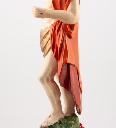 Zdjęcie nr 5: Rzeźba pełnoplastyczna, z tyłu opracowana, ustawiona na niewysokim cokole. Postać zwrócona frontalnie do widza, w kontrapoście, o esowato wygiętej sylwetce. W lewej ręce trzymał chorągiew, prawą unosi wysoko do góry w geście błogosławieństwa. Ciało o wyraźnie rzeźbionej muskulaturze z zaznaczonymi śladami męki. Twarz szczupła, o podkreślonej linii kości policzkowych i długim, prostym nosie, z dużymi oczami. Twarz okolona zarostem, włosy długie, gęste, z przedziałkiem na środku głowy, opadające na plecy. Przez biodra przepasane złote perizonium; pod szyją zapięty czerwony płaszcz opadający na plecy i lewe ramię. Karnacja ciała naturalistyczna, perizonium złocone.
