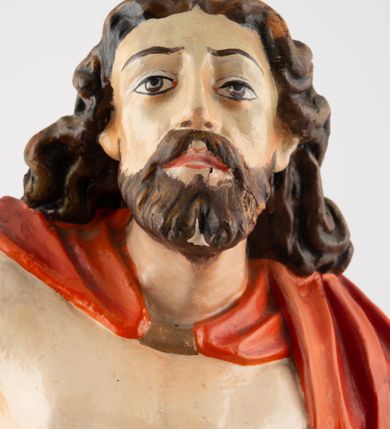 Zdjęcie nr 7: Rzeźba pełnoplastyczna, z tyłu opracowana, ustawiona na niewysokim cokole. Postać zwrócona frontalnie do widza, w kontrapoście, o esowato wygiętej sylwetce. W lewej ręce trzymał chorągiew, prawą unosi wysoko do góry w geście błogosławieństwa. Ciało o wyraźnie rzeźbionej muskulaturze z zaznaczonymi śladami męki. Twarz szczupła, o podkreślonej linii kości policzkowych i długim, prostym nosie, z dużymi oczami. Twarz okolona zarostem, włosy długie, gęste, z przedziałkiem na środku głowy, opadające na plecy. Przez biodra przepasane złote perizonium; pod szyją zapięty czerwony płaszcz opadający na plecy i lewe ramię. Karnacja ciała naturalistyczna, perizonium złocone.
