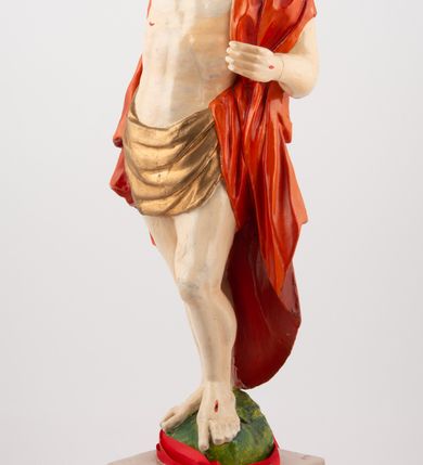 Zdjęcie nr 4: Rzeźba pełnoplastyczna, z tyłu opracowana, ustawiona na niewysokim cokole. Postać zwrócona frontalnie do widza, w kontrapoście, o esowato wygiętej sylwetce. W lewej ręce trzymał chorągiew, prawą unosi wysoko do góry w geście błogosławieństwa. Ciało o wyraźnie rzeźbionej muskulaturze z zaznaczonymi śladami męki. Twarz szczupła, o podkreślonej linii kości policzkowych i długim, prostym nosie, z dużymi oczami. Twarz okolona zarostem, włosy długie, gęste, z przedziałkiem na środku głowy, opadające na plecy. Przez biodra przepasane złote perizonium; pod szyją zapięty czerwony płaszcz opadający na plecy i lewe ramię. Karnacja ciała naturalistyczna, perizonium złocone.
