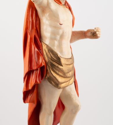 Zdjęcie nr 3: Rzeźba pełnoplastyczna, z tyłu opracowana, ustawiona na niewysokim cokole. Postać zwrócona frontalnie do widza, w kontrapoście, o esowato wygiętej sylwetce. W lewej ręce trzymał chorągiew, prawą unosi wysoko do góry w geście błogosławieństwa. Ciało o wyraźnie rzeźbionej muskulaturze z zaznaczonymi śladami męki. Twarz szczupła, o podkreślonej linii kości policzkowych i długim, prostym nosie, z dużymi oczami. Twarz okolona zarostem, włosy długie, gęste, z przedziałkiem na środku głowy, opadające na plecy. Przez biodra przepasane złote perizonium; pod szyją zapięty czerwony płaszcz opadający na plecy i lewe ramię. Karnacja ciała naturalistyczna, perizonium złocone.
