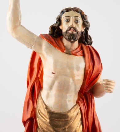 Zdjęcie nr 1: Rzeźba pełnoplastyczna, z tyłu opracowana, ustawiona na niewysokim cokole. Postać zwrócona frontalnie do widza, w kontrapoście, o esowato wygiętej sylwetce. W lewej ręce trzymał chorągiew, prawą unosi wysoko do góry w geście błogosławieństwa. Ciało o wyraźnie rzeźbionej muskulaturze z zaznaczonymi śladami męki. Twarz szczupła, o podkreślonej linii kości policzkowych i długim, prostym nosie, z dużymi oczami. Twarz okolona zarostem, włosy długie, gęste, z przedziałkiem na środku głowy, opadające na plecy. Przez biodra przepasane złote perizonium; pod szyją zapięty czerwony płaszcz opadający na plecy i lewe ramię. Karnacja ciała naturalistyczna, perizonium złocone.
