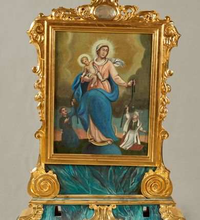 Zdjęcie nr 1: Pole obrazowe w formie stojącego prostokąta, ujęte profilowaną ramą oraz flankowane konsolami z podwieszonymi kampanulami przechodzącymi w spływy wolutowe stanowiące podstawę. Ramę wieńczy ornamentalny szczyt z akantu z owalnym kartuszem. Obraz na podstawie w formie profilowanego, zwężającego się ku górze cokołu, ujętego po bokach spływami wolutowymi, dekorowana fragmentami stylizowanej muszli, z dwoma otworami na drążki. 
Na awersie obraz Matki Boskiej z Dzieciątkiem i klęczącymi wiernymi. W centrum Maria stojąca na globie i sierpie księżyca, ukazana frontalnie, z głową skierowaną w lewo. Prawą ręką podtrzymuje Dzieciątko, lewą wyciąga w bok, trzymając pasek. Ubrana jest w różową suknię, przepasaną w talii, niebieski płaszcz przerzucony przez prawe ramię i zawinięty z przodu postaci, na głowie ma biały welon. Dzieciątko w pozycji siedzącej, zwrócone w trzech czwartych w lewo, przechylone w prawo, lewą ręką obejmuje Matkę, prawą wyciąga, w dłoni trzyma pasek. Ukazane jaki niemal nagie, przewiązane białą pieluszką. Po lewej stronie Marii klęczy kobieta, zwrócona w trzech czwartych w prawo, z uniesioną głową. Prawą wyciągniętą w górę ręką trzyma pasek, w lewej opuszczonej trzyma różaniec. Ubrana jest w białą koszulę, zielony gorset, czerwoną spódnicę z białą zapaską, na głowie ma biały czepek, na ramiona narzuconą białą chustę. Po prawej stronie Marii klęczy mężczyzna, zwrócony w trzech czwartych w lewo, z uniesioną głową. W lewej wyciągniętej w górę ręce trzyma pasek, w prawej ugiętej trzyma różaniec. Ma szczupłą twarz, krótkie, podgolone włosy oraz wąsy. Ubrany jest w niebieska sukmanę, przepasaną brązowym pasem, na nogach ma wysokie buty. Postacie ukazane na tle pejzażu z zachmurzonym niebem, rozjaśnionym wokół postaci Marii. 
Na rewersie całopostaciowe przestawienia św. Jadwigi i św. Floriana. W lewej części obrazu św. Jadwiga ukazana frontalnie, w kontrapoście, przechylona w lewo, obiema rekami podtrzymuje krucyfiks. Twarz ma pociągłą, o małych oczach, prostym nosie i pełnych ustach. Ubrana jest w czerwona suknię spodnią i jasnoniebieską suknię wierzchnią, przepasaną w talii. Na ramiona ma narzucony jasnobrązowy płaszcz z gronostajowa pelerynką, na głowie ma biały welon i zamkniętą koronę. W prawej części obrazu ukazany św. Florian, zwrócony w trzech czwartych w prawo, lekko pochylony, wlewej ręce trzyma drzewce chorągwi, w prawej wiaderko, z którego wylewa wodę na stojący poniżej palące się budynki. Twarz ma szczupłą, o małych oczach, garbatym nosie i małych ustach, okoloną krótkimi, brązowymi włosami i brodą. Ubrany jest w zieloną tunikę i zbroję, przez prawe ramię ma przerzucony jasnopomarańczowy płaszcz, na głowie ma hełm z pióropuszem. Postacie ukazane na tle pejzażu z zachmurzonym niebem, rozjaśnionym pośrodku. 








