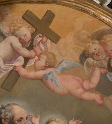 Zdjęcie nr 12: Owalny obraz, w drewnianej, profilowanej, złoconej ramie ukazuje klęczącego św. Józefa z siedzącym na chmurach Jezusem w towarzystwie grającego na kontrabasie anioła, grup uskrzydlonych puttów i główek anielskich. Józef ukazany jest w trzech czwartych, z lewą ręką obejmującą Jezusa, a prawą, zgiętą w łokciu i wyciągniętą do przodu. Głowa z łysiną czołową i siwymi, kręconymi, krótkimi włosami; twarz o rysach starszego mężczyzny, z krótkim nosem i otwartymi oczami. Święty ubrany jest w jasnofioletową suknię i brązowy płaszcz okrywający niemal cała sylwetkę. Siedzący na chmurze z trzema główkami aniołków nagi Jezus głowę zwraca ku górze i wysoko unosi rączki. Jego twarz jest pełna, policzki pękate, zaczerwienione, oczy ciemnobrązowe, krótki nosek i otwarte, pełne usta, włosy krótkie, jasne, kręcone.  Po prawej stronie klęczy anioł grający na kontrabasie, ukazany w trzech czwartych, zwrócony głową w prawo, ubrany w niebieską suknię odsłaniającą lewą pierś i bladoczerwony płaszcz. Jego głowa jest przedstawiona z profilu, z gęstymi, kręconymi, blond włosami, opadającymi na ramiona. Twarz ma pociągłą, z długim, zadartym nosem, otwartymi oczami i różowymi, otwartymi ustami. Przed św. Józefem siedzi para aniołków, z których jeden trzyma długi kij zakończony lilią. W górnej strefie wyłaniają się z chmur główki aniołków i dwa uskrzydlone aniołki trzymające krzyż. Tło nieokreślone, w tonacjach szarości, z widoczną dolną częścią kolumny. 
