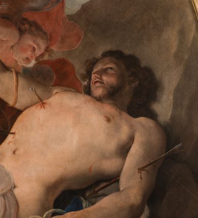 Zdjęcie nr 16: Obraz w kształcie owalu, w profilowanej, złoconej ramie ukazuje na wpół leżącego na skale, niemal nagiego św. Sebastiana przebitego strzałami w towarzystwie uskrzydlonych aniołków. Święty ukazany w trzech czwartych, z silnie wysklepioną klatką piersiową, głowę zwraca ku górze. Jego prawą, uniesioną rękę podtrzymuje anioł, lewa ręka spoczywa na skale. Biodra zasłania biała, zakrwawiona chusta, a na skale rozpostarta jest niebieska szata. Na nogach i rękach widoczne resztki krępujących go sznurów. Ciało przebijają trzy strzały, dwie w klatce piersiowej, jedna w lewym ramieniu. Za świętym trzy nagie niemalże aniołki w zróżnicowanych pozach, z których jeden trzyma palmę męczeństwa; anioły ukazane szkicowo, na tle czerwonej, rozłożystej tkaniny. W tle skłębione niebieskie chmury i szaro-brązowa nieokreślona przestrzeń. Po lewej, u dołu sygnatura „Paolo Pagani Pinxit&quot;.