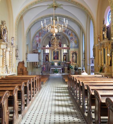 Zdjęcie nr 55: Kościół murowany, orientowany, jednonawowy, trójprzęsłowy, z transeptem i jednoprzęsłowym, węższym i niższym prezbiterium zamkniętym trójbocznie. Między nawą a transeptem po obu stronach znajdują się kruchty, do prezbiterium od strony północnej dostawiona kruchta złożona z dwóch lokalności. Ściany są rozczłonkowane filarami, tworzącymi płytkie arkadowe wnęki. Między nawą a prezbiterium arkada tęczowa. Sklepienie krzyżowe na gurtach spływających na filary. Prezbiterium oświetlają wąskie, prostokątne okna zamknięte ostrołukowo, w nawie i w transepcie znajdują się prostokątne okna prostokątne zamknięte półkoliście, w ścianie frontowej w dolnej części okna prostokątne zamknięte półkoliście, a w górnej podwójne okna prostokątne. Fasada ujęta dwiema narożnymi szkarpami, zwieńczona trójkątnie. Do niej dostawiona kruchta z dwuspadowym daszkiem i wejściem w kształcie prostokąta zamkniętego półkoliście. W kamiennej fasadzie znajdują się dołem okna prostokątne, zamknięte półkoliście, a górą  prostokątne, biforialne okna z nadprożem łukowatym wykonanym z cegły. Szczyt ceglany, podzielony na trzy strefy kamiennym wątkiem, z pięcioma wnękami prostokątnymi, zamkniętymi półkoliście, z wąskimi otworami w dolnej strefie i z owalnym oknem w drugiej. Elewacje boczne nawy ujęte skarpami. Dachy dwuspadowe, kryte dachówką, z wieżyczką na sygnaturkę.         