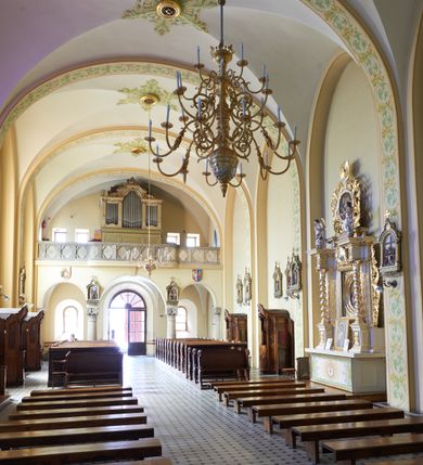 Zdjęcie nr 61: Kościół murowany, orientowany, jednonawowy, trójprzęsłowy, z transeptem i jednoprzęsłowym, węższym i niższym prezbiterium zamkniętym trójbocznie. Między nawą a transeptem po obu stronach znajdują się kruchty, do prezbiterium od strony północnej dostawiona kruchta złożona z dwóch lokalności. Ściany są rozczłonkowane filarami, tworzącymi płytkie arkadowe wnęki. Między nawą a prezbiterium arkada tęczowa. Sklepienie krzyżowe na gurtach spływających na filary. Prezbiterium oświetlają wąskie, prostokątne okna zamknięte ostrołukowo, w nawie i w transepcie znajdują się prostokątne okna prostokątne zamknięte półkoliście, w ścianie frontowej w dolnej części okna prostokątne zamknięte półkoliście, a w górnej podwójne okna prostokątne. Fasada ujęta dwiema narożnymi szkarpami, zwieńczona trójkątnie. Do niej dostawiona kruchta z dwuspadowym daszkiem i wejściem w kształcie prostokąta zamkniętego półkoliście. W kamiennej fasadzie znajdują się dołem okna prostokątne, zamknięte półkoliście, a górą  prostokątne, biforialne okna z nadprożem łukowatym wykonanym z cegły. Szczyt ceglany, podzielony na trzy strefy kamiennym wątkiem, z pięcioma wnękami prostokątnymi, zamkniętymi półkoliście, z wąskimi otworami w dolnej strefie i z owalnym oknem w drugiej. Elewacje boczne nawy ujęte skarpami. Dachy dwuspadowe, kryte dachówką, z wieżyczką na sygnaturkę.         