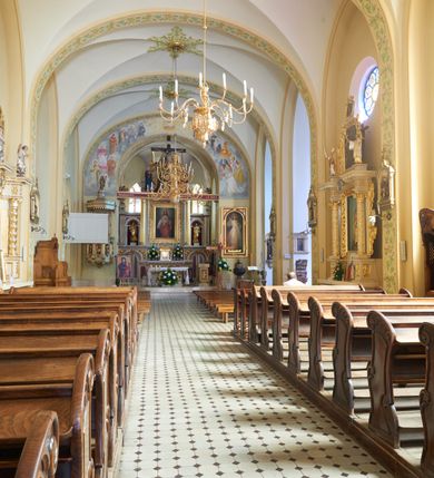 Zdjęcie nr 58: Kościół murowany, orientowany, jednonawowy, trójprzęsłowy, z transeptem i jednoprzęsłowym, węższym i niższym prezbiterium zamkniętym trójbocznie. Między nawą a transeptem po obu stronach znajdują się kruchty, do prezbiterium od strony północnej dostawiona kruchta złożona z dwóch lokalności. Ściany są rozczłonkowane filarami, tworzącymi płytkie arkadowe wnęki. Między nawą a prezbiterium arkada tęczowa. Sklepienie krzyżowe na gurtach spływających na filary. Prezbiterium oświetlają wąskie, prostokątne okna zamknięte ostrołukowo, w nawie i w transepcie znajdują się prostokątne okna prostokątne zamknięte półkoliście, w ścianie frontowej w dolnej części okna prostokątne zamknięte półkoliście, a w górnej podwójne okna prostokątne. Fasada ujęta dwiema narożnymi szkarpami, zwieńczona trójkątnie. Do niej dostawiona kruchta z dwuspadowym daszkiem i wejściem w kształcie prostokąta zamkniętego półkoliście. W kamiennej fasadzie znajdują się dołem okna prostokątne, zamknięte półkoliście, a górą  prostokątne, biforialne okna z nadprożem łukowatym wykonanym z cegły. Szczyt ceglany, podzielony na trzy strefy kamiennym wątkiem, z pięcioma wnękami prostokątnymi, zamkniętymi półkoliście, z wąskimi otworami w dolnej strefie i z owalnym oknem w drugiej. Elewacje boczne nawy ujęte skarpami. Dachy dwuspadowe, kryte dachówką, z wieżyczką na sygnaturkę.         