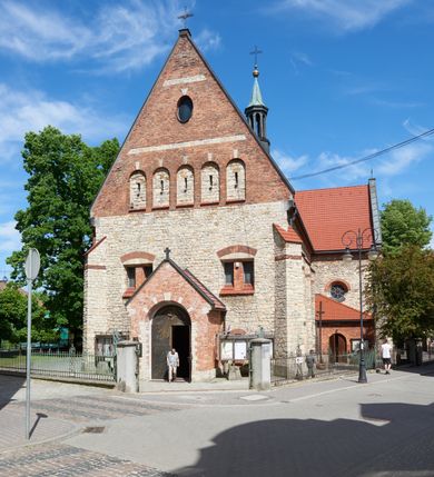 Zdjęcie nr 2: Kościół murowany, orientowany, jednonawowy, trójprzęsłowy, z transeptem i jednoprzęsłowym, węższym i niższym prezbiterium zamkniętym trójbocznie. Między nawą a transeptem po obu stronach znajdują się kruchty, do prezbiterium od strony północnej dostawiona kruchta złożona z dwóch lokalności. Ściany są rozczłonkowane filarami, tworzącymi płytkie arkadowe wnęki. Między nawą a prezbiterium arkada tęczowa. Sklepienie krzyżowe na gurtach spływających na filary. Prezbiterium oświetlają wąskie, prostokątne okna zamknięte ostrołukowo, w nawie i w transepcie znajdują się prostokątne okna prostokątne zamknięte półkoliście, w ścianie frontowej w dolnej części okna prostokątne zamknięte półkoliście, a w górnej podwójne okna prostokątne. Fasada ujęta dwiema narożnymi szkarpami, zwieńczona trójkątnie. Do niej dostawiona kruchta z dwuspadowym daszkiem i wejściem w kształcie prostokąta zamkniętego półkoliście. W kamiennej fasadzie znajdują się dołem okna prostokątne, zamknięte półkoliście, a górą  prostokątne, biforialne okna z nadprożem łukowatym wykonanym z cegły. Szczyt ceglany, podzielony na trzy strefy kamiennym wątkiem, z pięcioma wnękami prostokątnymi, zamkniętymi półkoliście, z wąskimi otworami w dolnej strefie i z owalnym oknem w drugiej. Elewacje boczne nawy ujęte skarpami. Dachy dwuspadowe, kryte dachówką, z wieżyczką na sygnaturkę.         
