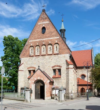 Zdjęcie nr 1: Kościół murowany, orientowany, jednonawowy, trójprzęsłowy, z transeptem i jednoprzęsłowym, węższym i niższym prezbiterium zamkniętym trójbocznie. Między nawą a transeptem po obu stronach znajdują się kruchty, do prezbiterium od strony północnej dostawiona kruchta złożona z dwóch lokalności. Ściany są rozczłonkowane filarami, tworzącymi płytkie arkadowe wnęki. Między nawą a prezbiterium arkada tęczowa. Sklepienie krzyżowe na gurtach spływających na filary. Prezbiterium oświetlają wąskie, prostokątne okna zamknięte ostrołukowo, w nawie i w transepcie znajdują się prostokątne okna prostokątne zamknięte półkoliście, w ścianie frontowej w dolnej części okna prostokątne zamknięte półkoliście, a w górnej podwójne okna prostokątne. Fasada ujęta dwiema narożnymi szkarpami, zwieńczona trójkątnie. Do niej dostawiona kruchta z dwuspadowym daszkiem i wejściem w kształcie prostokąta zamkniętego półkoliście. W kamiennej fasadzie znajdują się dołem okna prostokątne, zamknięte półkoliście, a górą  prostokątne, biforialne okna z nadprożem łukowatym wykonanym z cegły. Szczyt ceglany, podzielony na trzy strefy kamiennym wątkiem, z pięcioma wnękami prostokątnymi, zamkniętymi półkoliście, z wąskimi otworami w dolnej strefie i z owalnym oknem w drugiej. Elewacje boczne nawy ujęte skarpami. Dachy dwuspadowe, kryte dachówką, z wieżyczką na sygnaturkę.         