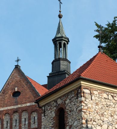 Zdjęcie nr 3: Kościół murowany, orientowany, jednonawowy, trójprzęsłowy, z transeptem i jednoprzęsłowym, węższym i niższym prezbiterium zamkniętym trójbocznie. Między nawą a transeptem po obu stronach znajdują się kruchty, do prezbiterium od strony północnej dostawiona kruchta złożona z dwóch lokalności. Ściany są rozczłonkowane filarami, tworzącymi płytkie arkadowe wnęki. Między nawą a prezbiterium arkada tęczowa. Sklepienie krzyżowe na gurtach spływających na filary. Prezbiterium oświetlają wąskie, prostokątne okna zamknięte ostrołukowo, w nawie i w transepcie znajdują się prostokątne okna prostokątne zamknięte półkoliście, w ścianie frontowej w dolnej części okna prostokątne zamknięte półkoliście, a w górnej podwójne okna prostokątne. Fasada ujęta dwiema narożnymi szkarpami, zwieńczona trójkątnie. Do niej dostawiona kruchta z dwuspadowym daszkiem i wejściem w kształcie prostokąta zamkniętego półkoliście. W kamiennej fasadzie znajdują się dołem okna prostokątne, zamknięte półkoliście, a górą  prostokątne, biforialne okna z nadprożem łukowatym wykonanym z cegły. Szczyt ceglany, podzielony na trzy strefy kamiennym wątkiem, z pięcioma wnękami prostokątnymi, zamkniętymi półkoliście, z wąskimi otworami w dolnej strefie i z owalnym oknem w drugiej. Elewacje boczne nawy ujęte skarpami. Dachy dwuspadowe, kryte dachówką, z wieżyczką na sygnaturkę.         