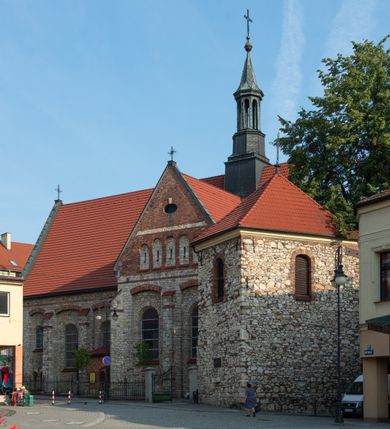 Zdjęcie nr 57: Kościół murowany, orientowany, jednonawowy, trójprzęsłowy, z transeptem i jednoprzęsłowym, węższym i niższym prezbiterium zamkniętym trójbocznie. Między nawą a transeptem po obu stronach znajdują się kruchty, do prezbiterium od strony północnej dostawiona kruchta złożona z dwóch lokalności. Ściany są rozczłonkowane filarami, tworzącymi płytkie arkadowe wnęki. Między nawą a prezbiterium arkada tęczowa. Sklepienie krzyżowe na gurtach spływających na filary. Prezbiterium oświetlają wąskie, prostokątne okna zamknięte ostrołukowo, w nawie i w transepcie znajdują się prostokątne okna prostokątne zamknięte półkoliście, w ścianie frontowej w dolnej części okna prostokątne zamknięte półkoliście, a w górnej podwójne okna prostokątne. Fasada ujęta dwiema narożnymi szkarpami, zwieńczona trójkątnie. Do niej dostawiona kruchta z dwuspadowym daszkiem i wejściem w kształcie prostokąta zamkniętego półkoliście. W kamiennej fasadzie znajdują się dołem okna prostokątne, zamknięte półkoliście, a górą  prostokątne, biforialne okna z nadprożem łukowatym wykonanym z cegły. Szczyt ceglany, podzielony na trzy strefy kamiennym wątkiem, z pięcioma wnękami prostokątnymi, zamkniętymi półkoliście, z wąskimi otworami w dolnej strefie i z owalnym oknem w drugiej. Elewacje boczne nawy ujęte skarpami. Dachy dwuspadowe, kryte dachówką, z wieżyczką na sygnaturkę.         