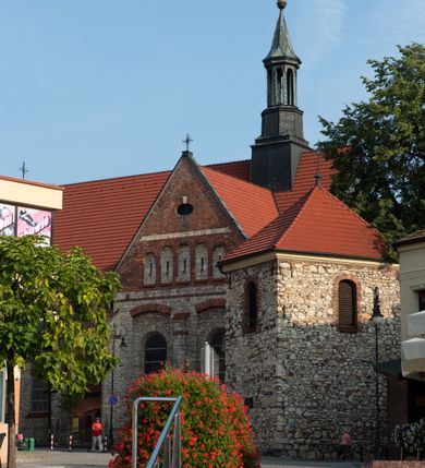 Zdjęcie nr 62: Kościół murowany, orientowany, jednonawowy, trójprzęsłowy, z transeptem i jednoprzęsłowym, węższym i niższym prezbiterium zamkniętym trójbocznie. Między nawą a transeptem po obu stronach znajdują się kruchty, do prezbiterium od strony północnej dostawiona kruchta złożona z dwóch lokalności. Ściany są rozczłonkowane filarami, tworzącymi płytkie arkadowe wnęki. Między nawą a prezbiterium arkada tęczowa. Sklepienie krzyżowe na gurtach spływających na filary. Prezbiterium oświetlają wąskie, prostokątne okna zamknięte ostrołukowo, w nawie i w transepcie znajdują się prostokątne okna prostokątne zamknięte półkoliście, w ścianie frontowej w dolnej części okna prostokątne zamknięte półkoliście, a w górnej podwójne okna prostokątne. Fasada ujęta dwiema narożnymi szkarpami, zwieńczona trójkątnie. Do niej dostawiona kruchta z dwuspadowym daszkiem i wejściem w kształcie prostokąta zamkniętego półkoliście. W kamiennej fasadzie znajdują się dołem okna prostokątne, zamknięte półkoliście, a górą  prostokątne, biforialne okna z nadprożem łukowatym wykonanym z cegły. Szczyt ceglany, podzielony na trzy strefy kamiennym wątkiem, z pięcioma wnękami prostokątnymi, zamkniętymi półkoliście, z wąskimi otworami w dolnej strefie i z owalnym oknem w drugiej. Elewacje boczne nawy ujęte skarpami. Dachy dwuspadowe, kryte dachówką, z wieżyczką na sygnaturkę.         